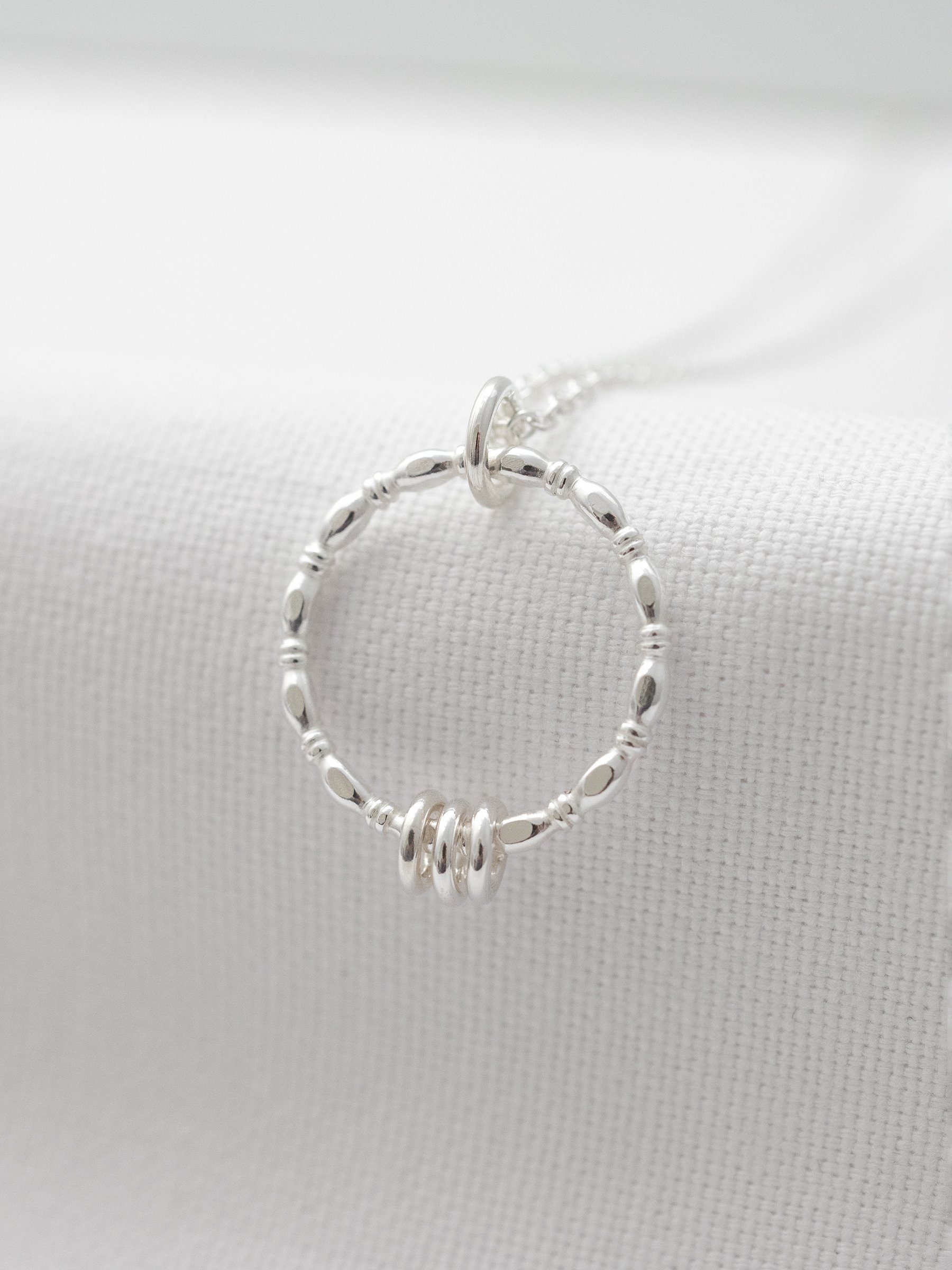 A close up of a sterling silver three ring necklace displayed over white material.