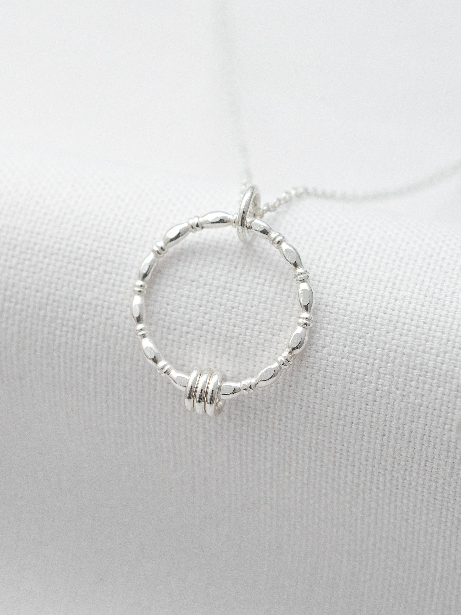 A silver 30th birthday ring necklace displayed over white material.