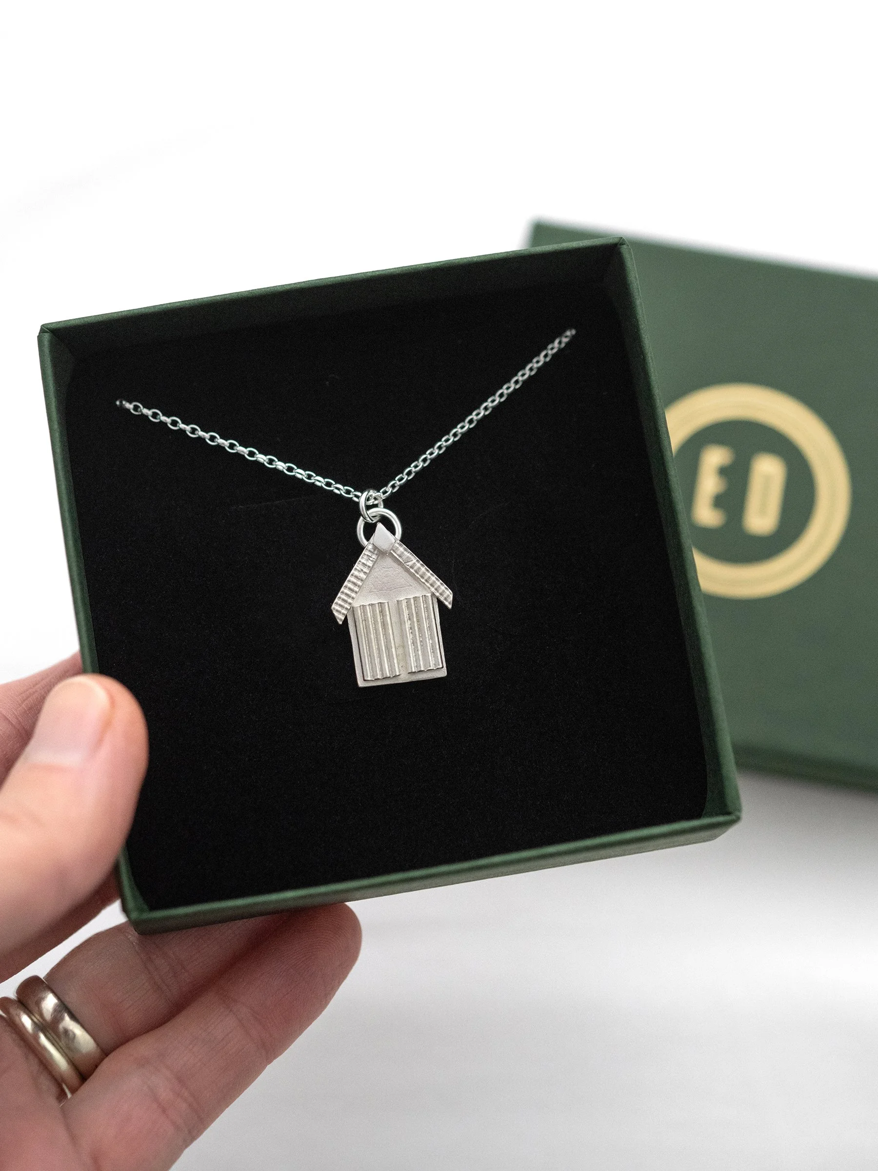 A silver beach hut necklace displayed in an Elizabeth Designs jewellery presentation box.