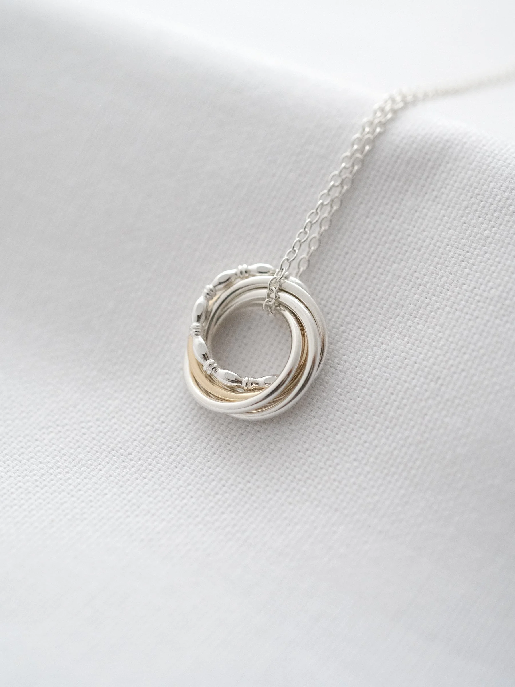 Hallmarked gold and silver five ring necklace displayed on white material.