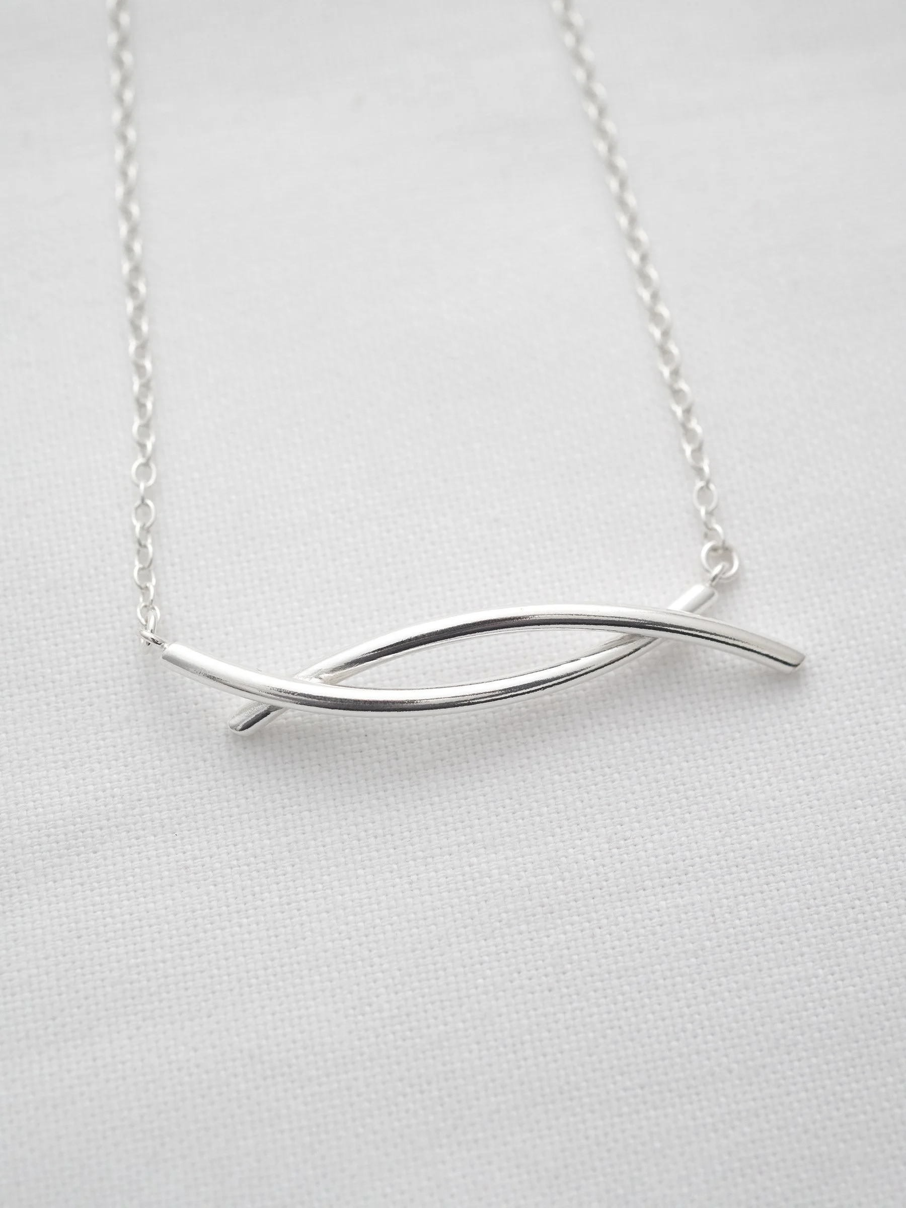 A sterling silver twist necklace displayed on white material.