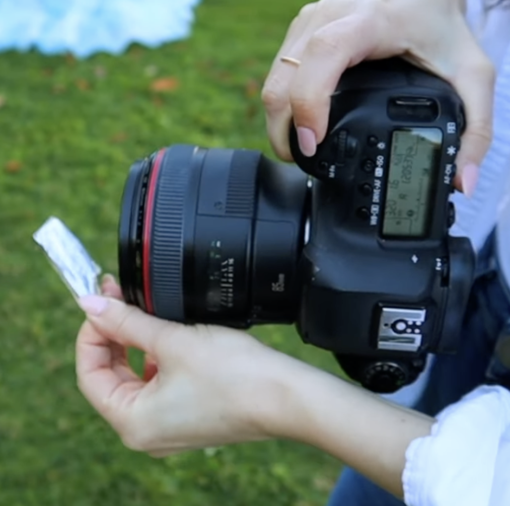 Demonstration of holding a reflective metallic object in front of a camera lens to create custom light flares and haze during a portrait shoot.
