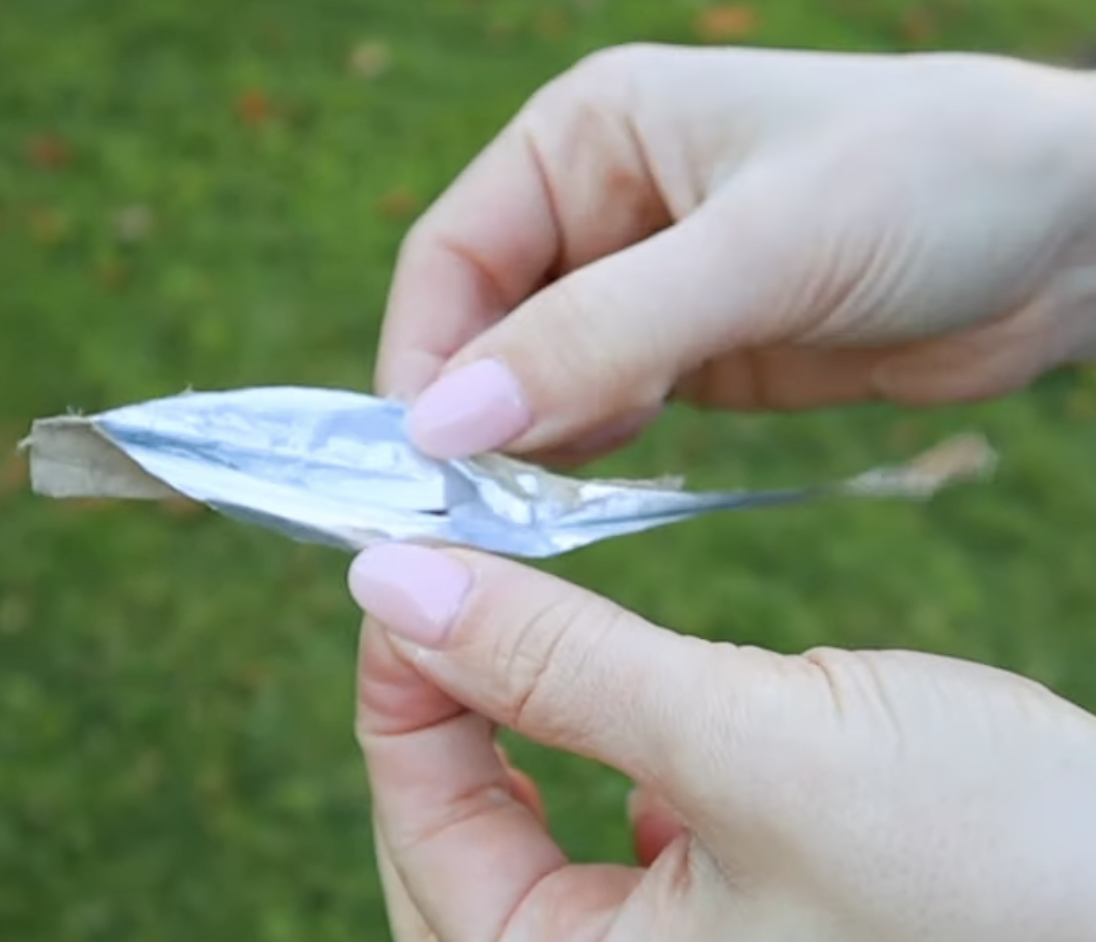 Close-up of a hand holding a piece of found metallic silver trash, demonstrating a resource for creative reflective photography props.