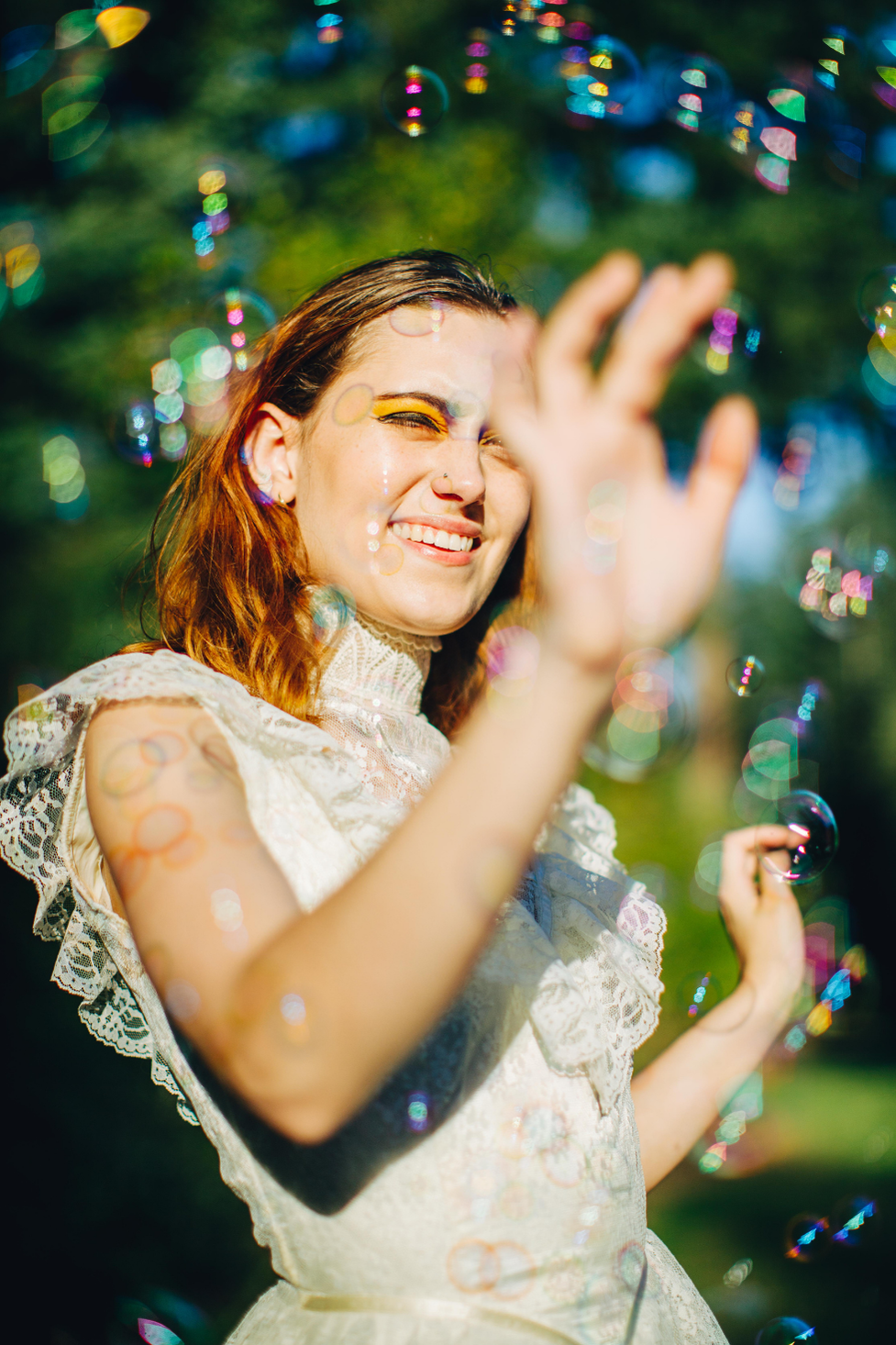 A creative portrait shot in direct sunlight using a bubble machine to add rainbow colors, texture, and shine to the frame.