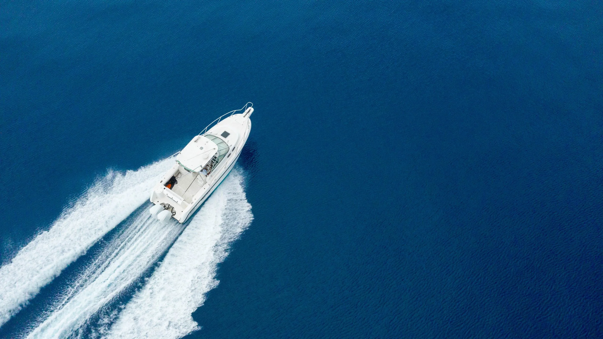 A white motorboat moving quickly across deep blue water, leaving a foamy wake behind.