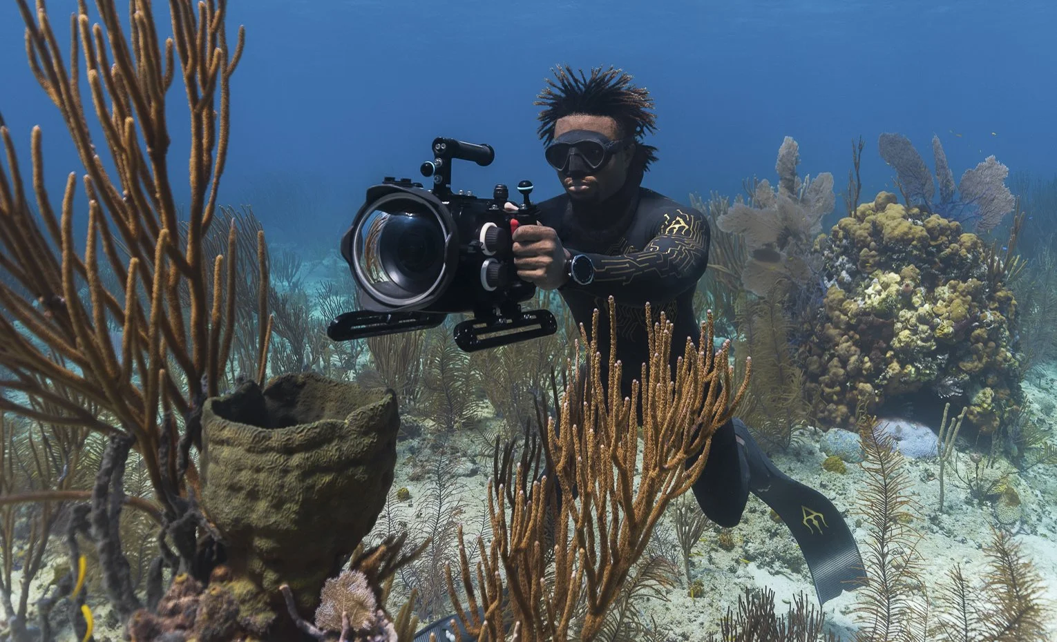 A scuba diver with a camera under the sea among coral reefs and marine life.