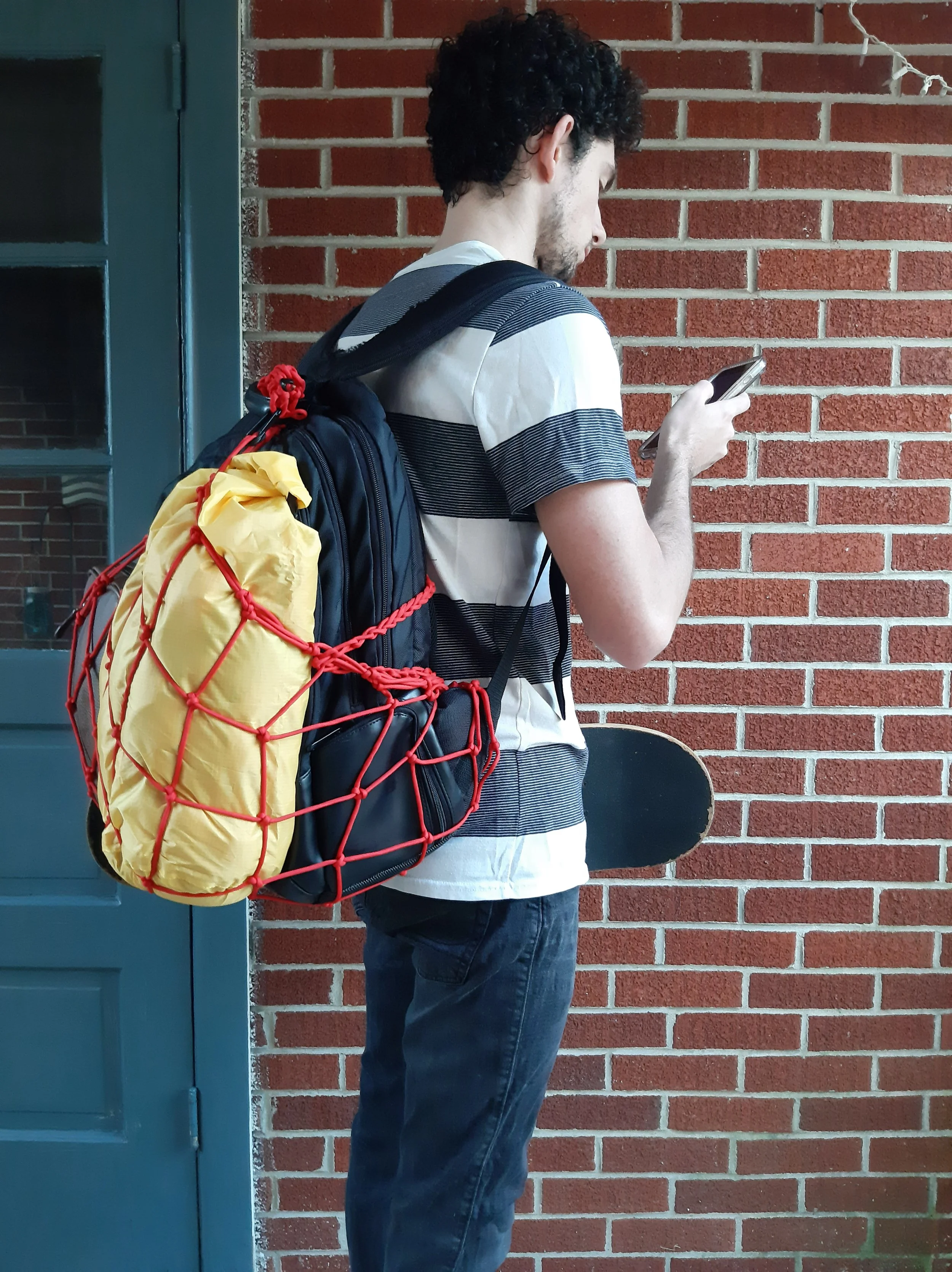 kid with the All-American backpack net holding a cell phone and skateboard.