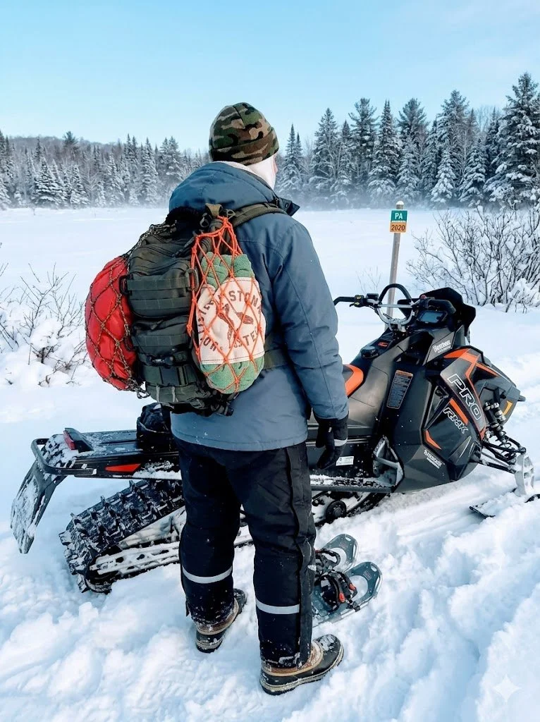 two Mini OPSnet backpack nets on a OD green molle backpack next to a snowmobile in the snow trails