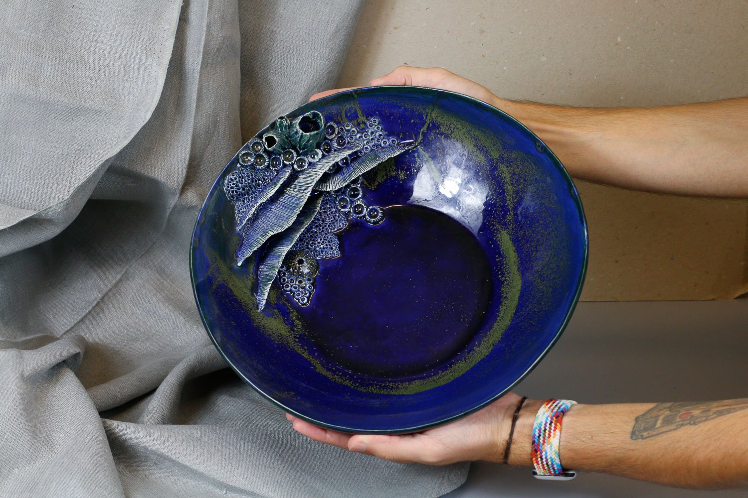 Taça azul forte com pormenores de recifes em cerâmica, segurada pelas mãos do artista