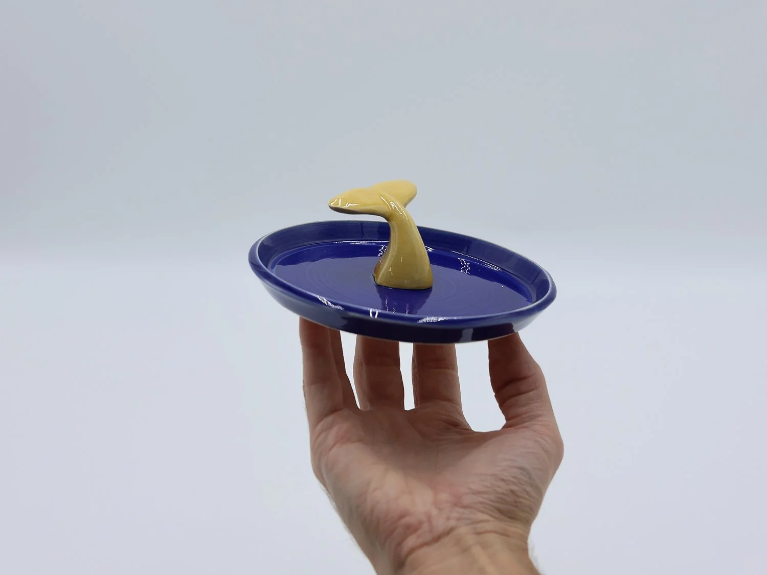 Mão a segurar prato em cerâmica, com cauda cor de mel no centro, feito à mão na cor azul azulejo