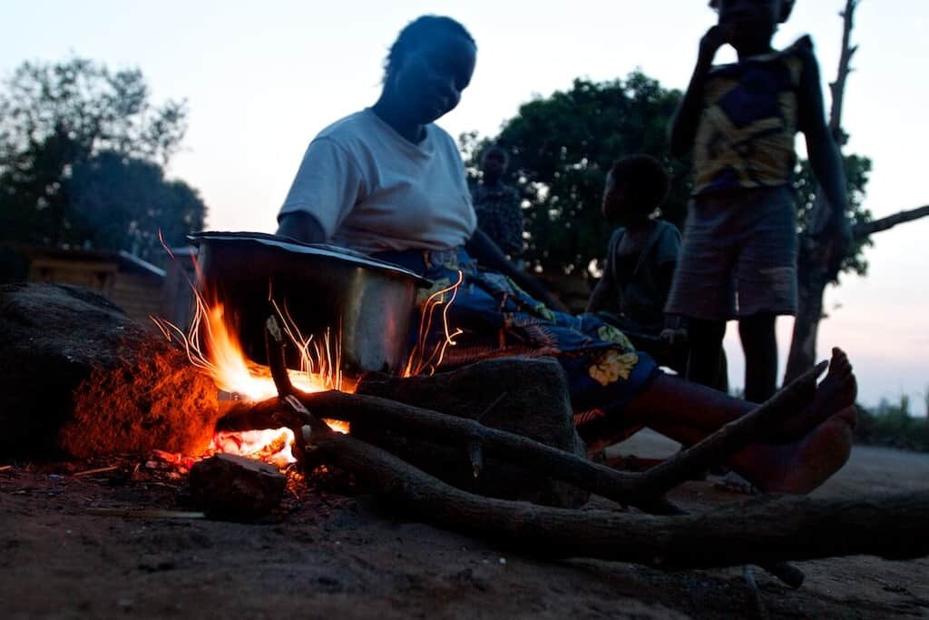   A woman cooks dinner for her family over a three-stone fire, which are very common in rural Africa, though neither efficient nor healthy. They require large amounts of wood for fuel, deepening the issue of deforestation. Using wood also produces sm