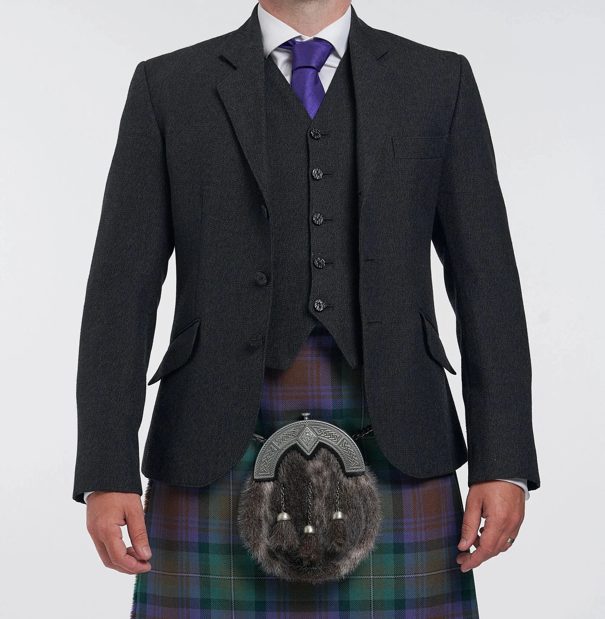 Man wearing a dark gray suit jacket, matching vest, white shirt, purple tie, and a traditional Scottish kilt with a sporran.