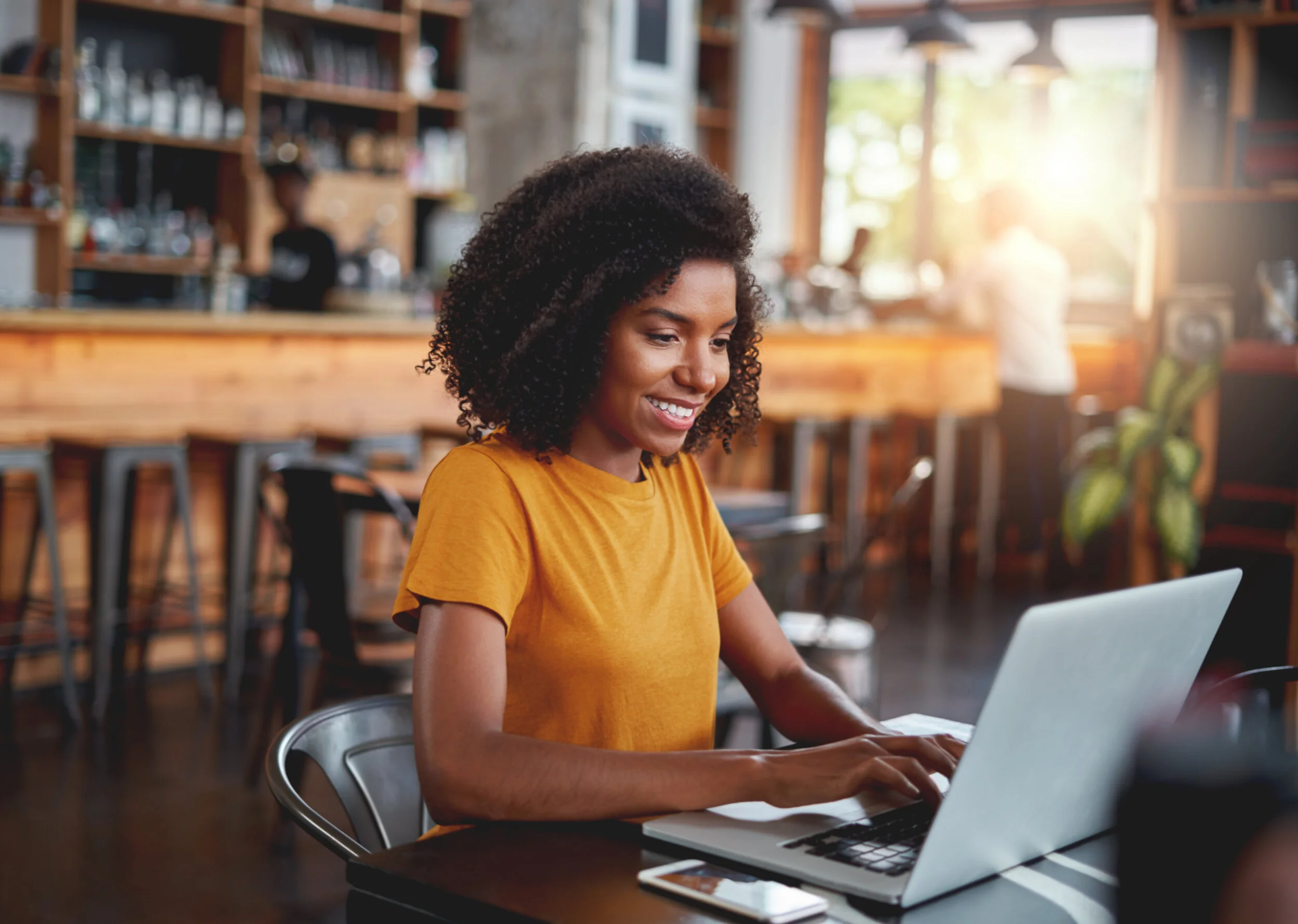 Woman sitting in a coffee shop smiling while working on her computer
