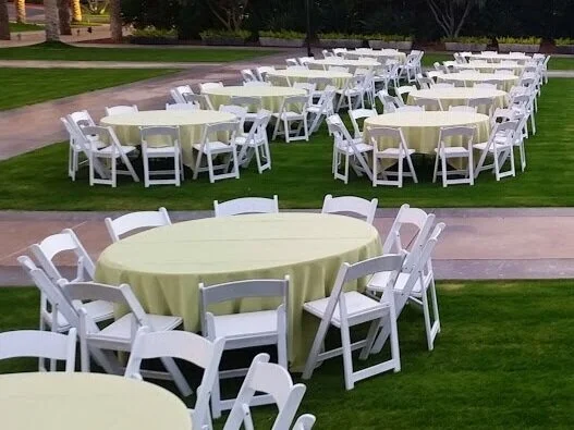 White folding chairs and round tables with linens on a lawn