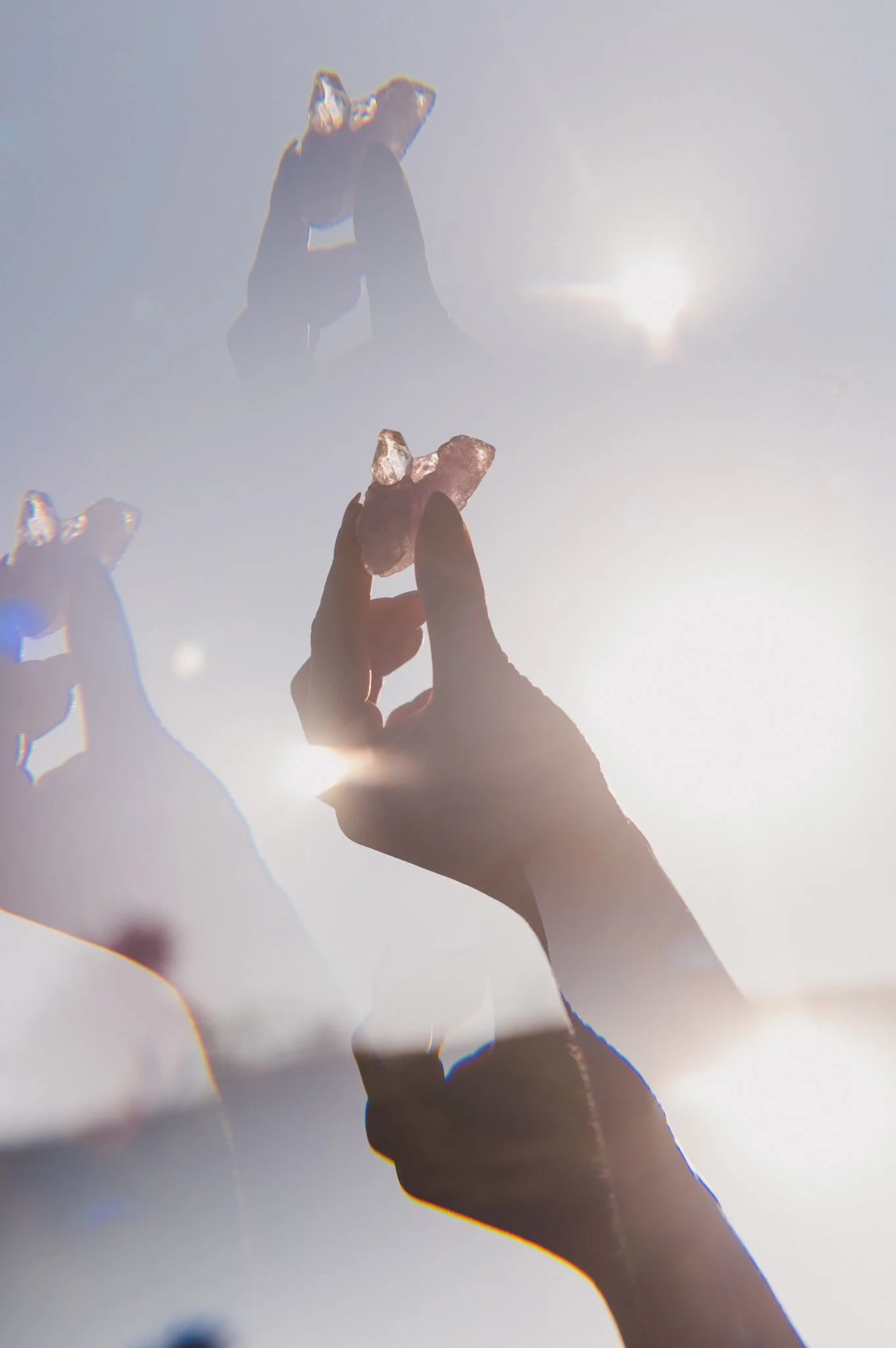 Silhouette of a hand holding a crystal against a bright sky, creating a dreamy, ethereal effect with light reflections.