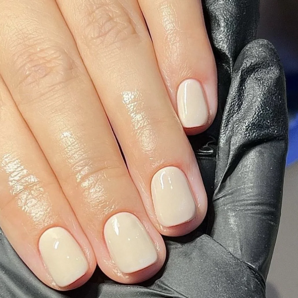 Close-up of a hand with neatly manicured fingernails painted in light cream color, resting on a black leather glove.