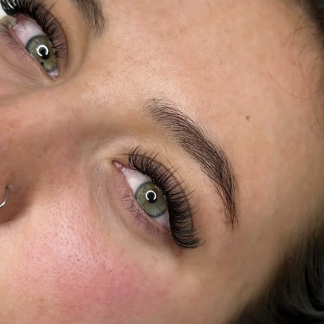 Close-up of a person's eyes with long eyelashes and neatly shaped eyebrows.