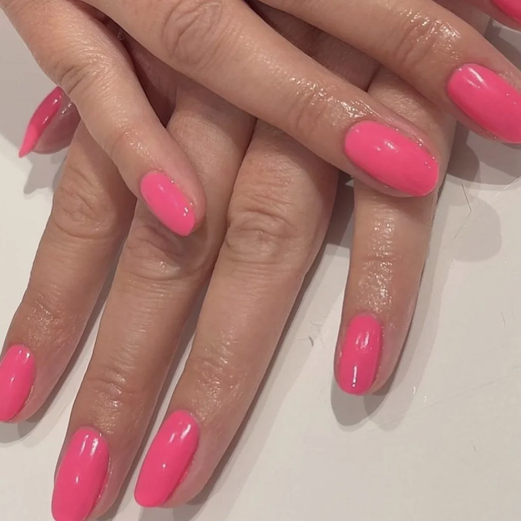 Close-up of hands with shiny, bright pink manicured nails.