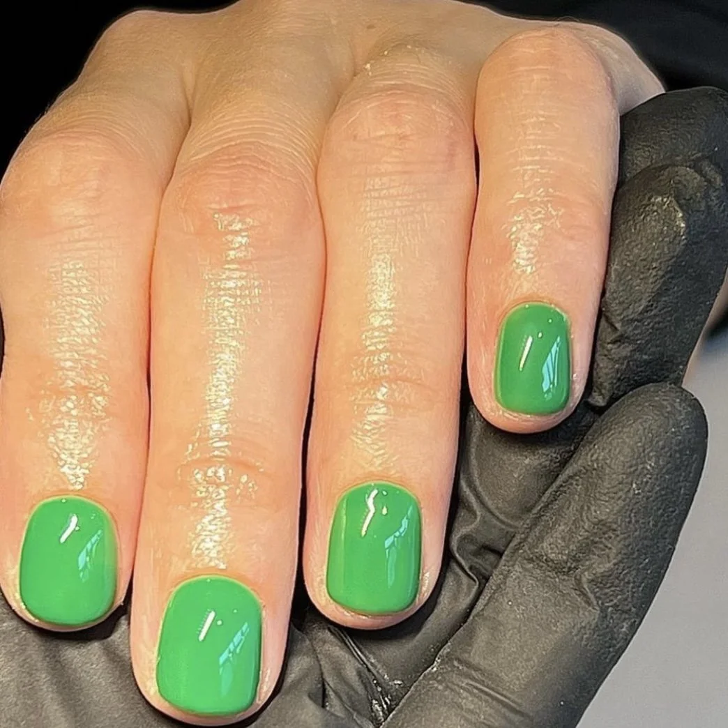 Close-up of a hand with bright green nail polish on all fingernails, held by a person wearing a black glove.