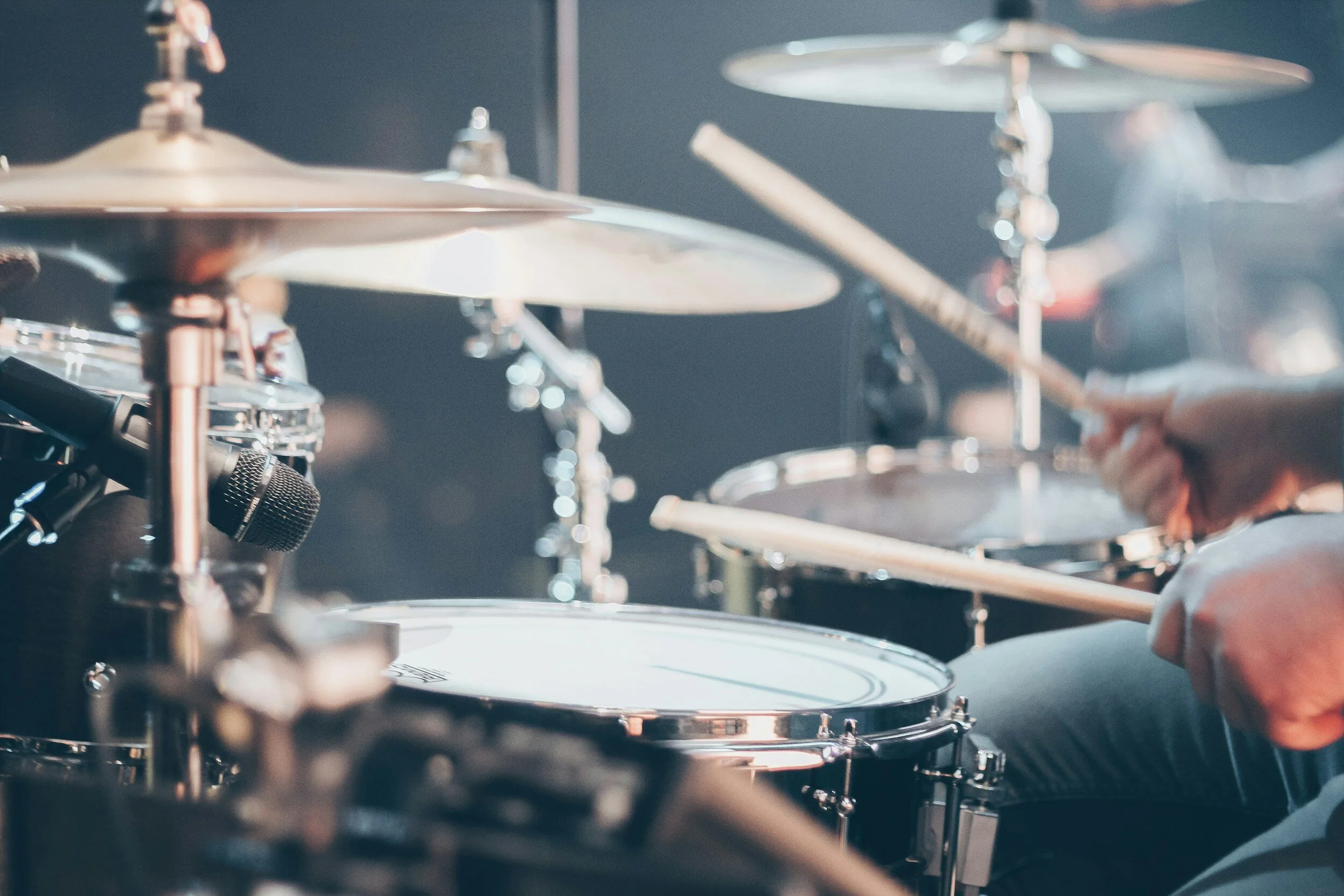 Close-up of a drummer playing a drum kit with cymbals, drums, and drumsticks visible.