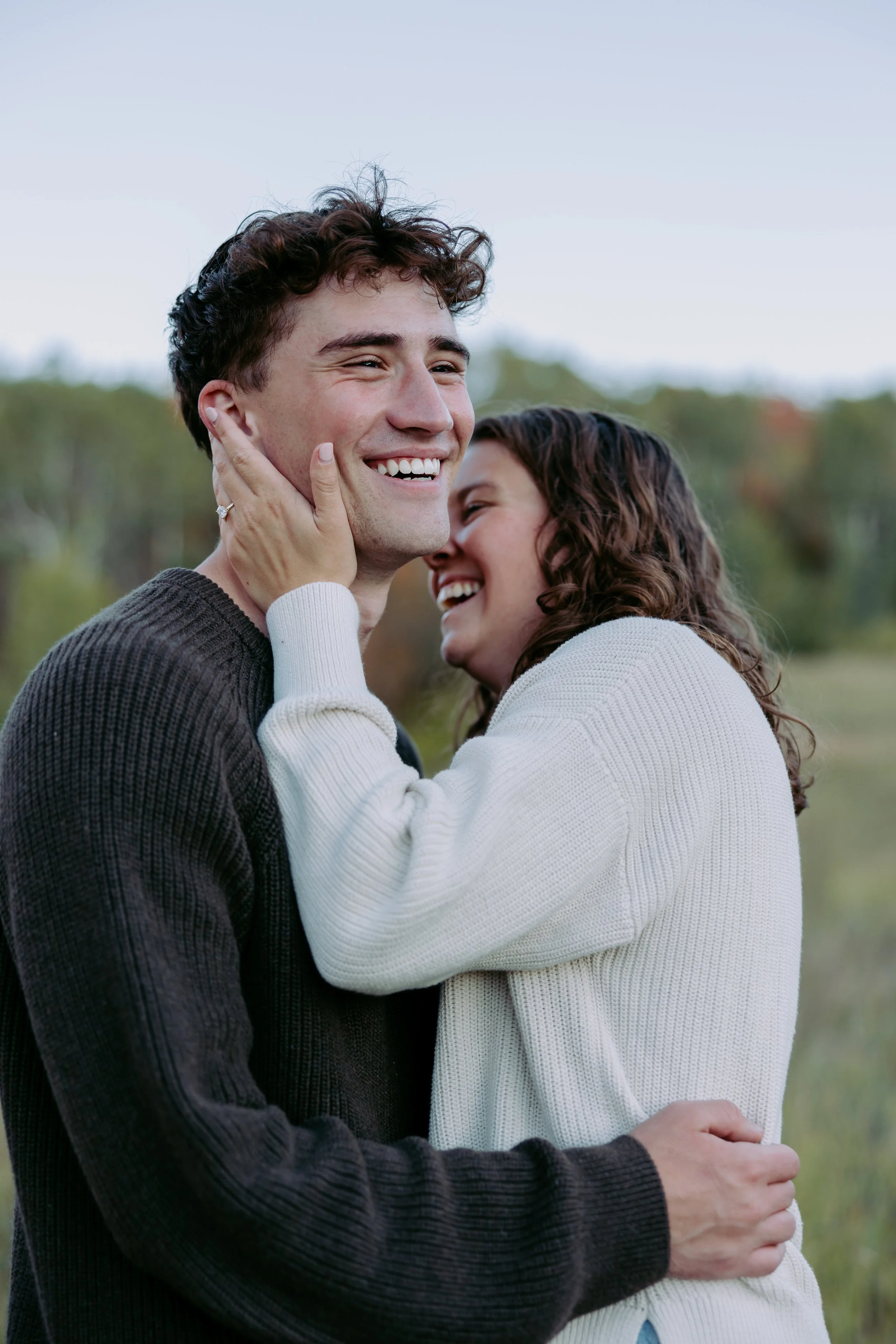 A happy couple embracing outdoors with a man smiling and a woman holding his face.