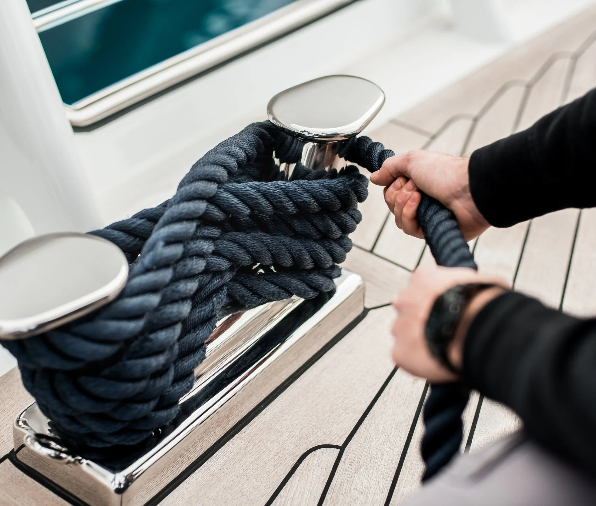 Detail of hands cleating off superyacht mooring lines on the foredeck with teak deck and stainless steel fittings