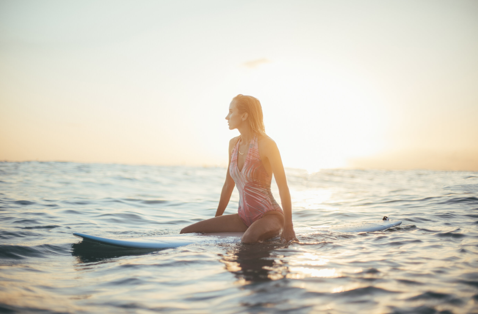 Woman sitting on a surfboard in the ocean at sunset