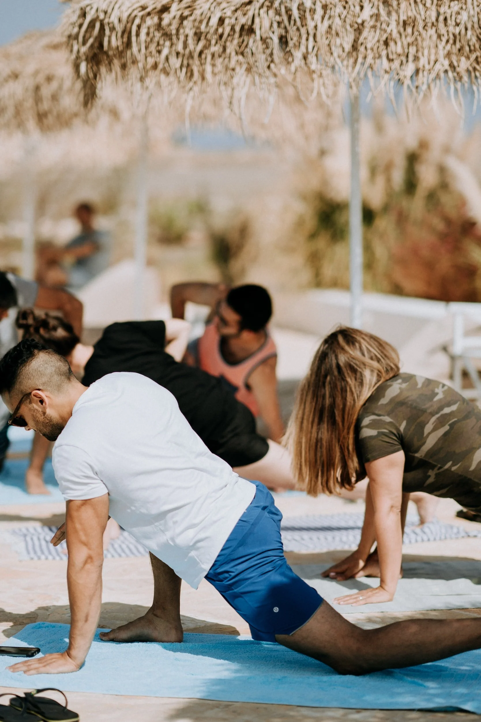 People practicing yoga under straw umbrellas on a sunny beach day.