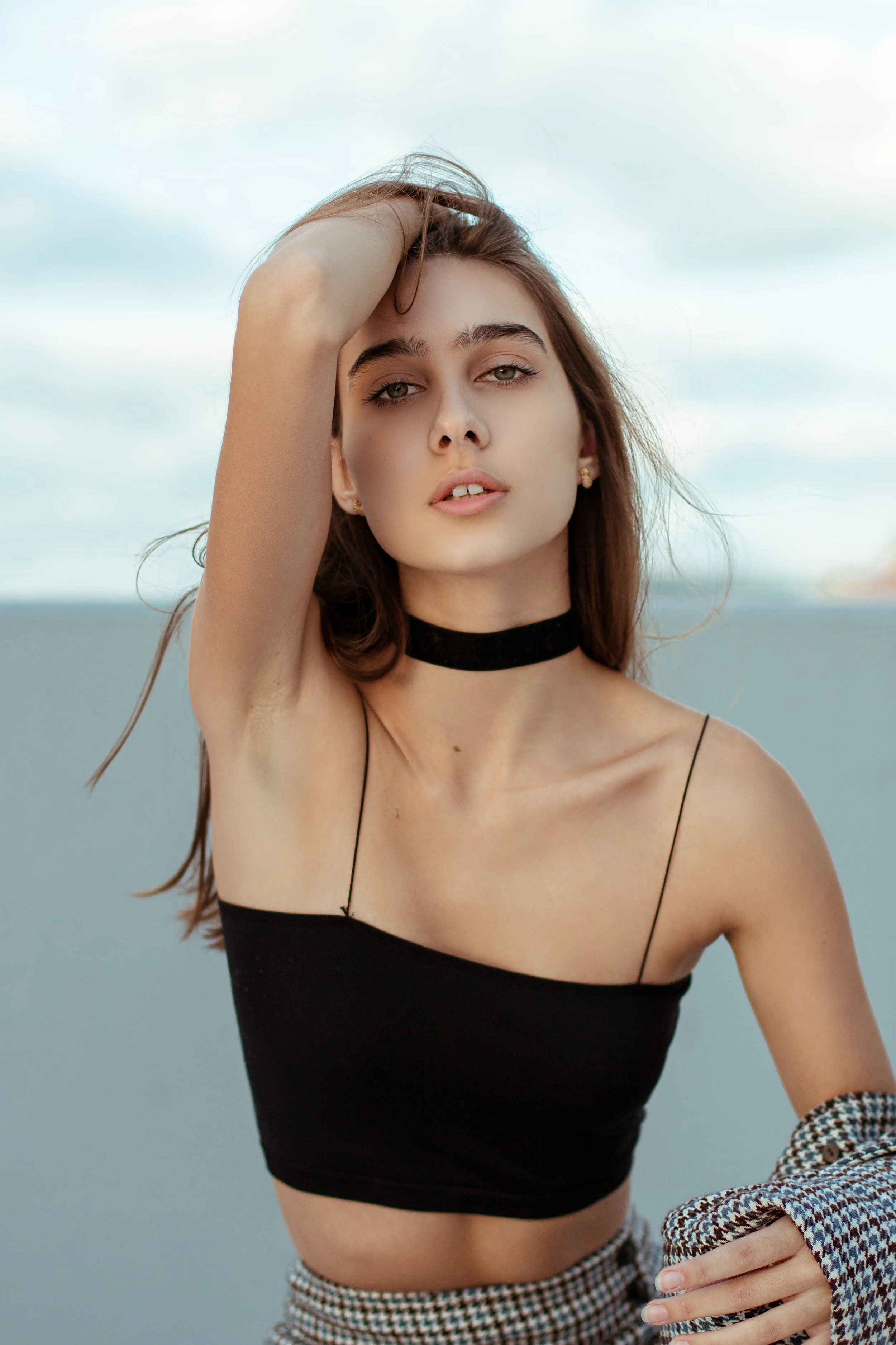 A person posing with one arm raised, wearing a black sleeveless top and checkered pants.