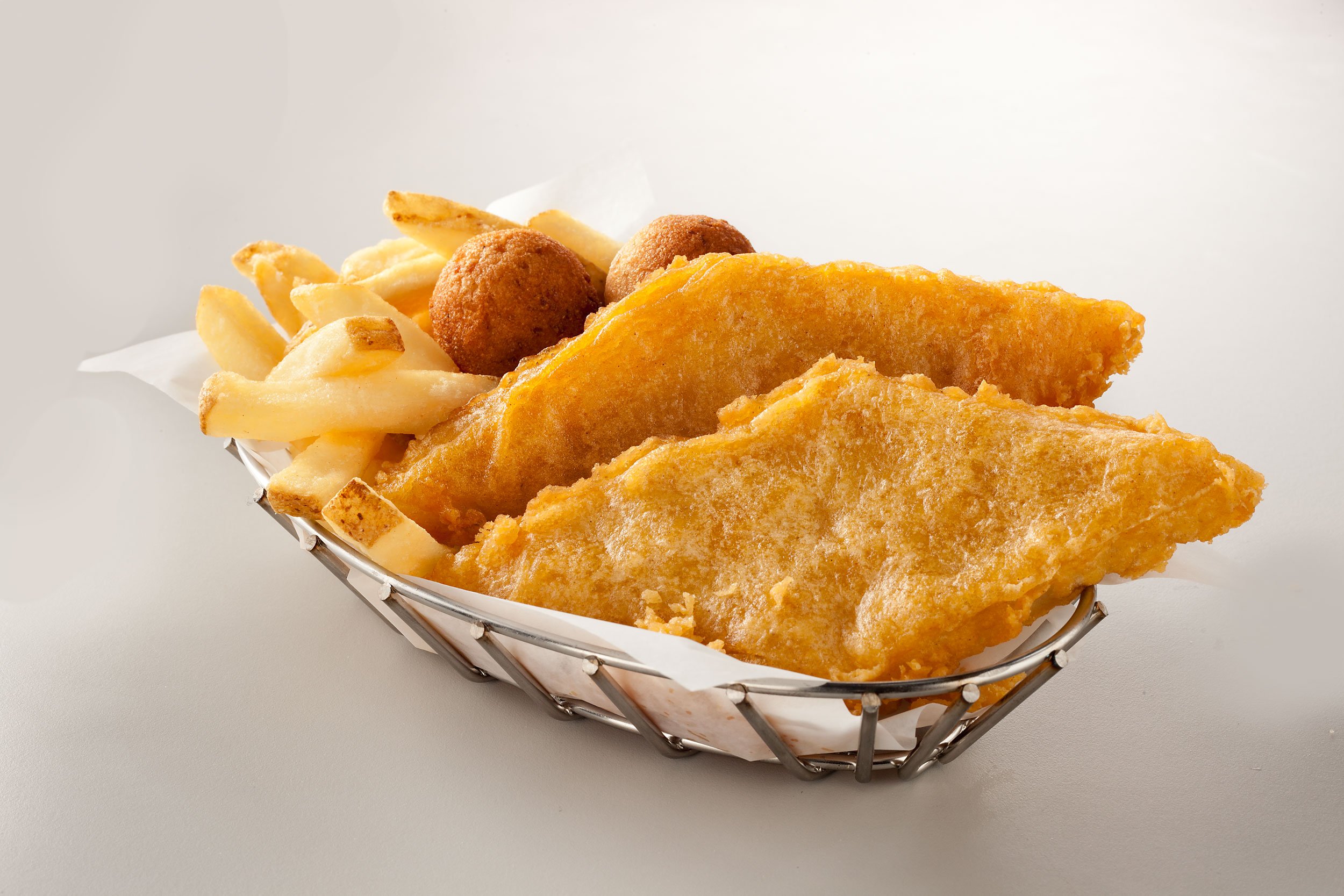 Fried fish and french fries in a basket with hushpuppies on the side.