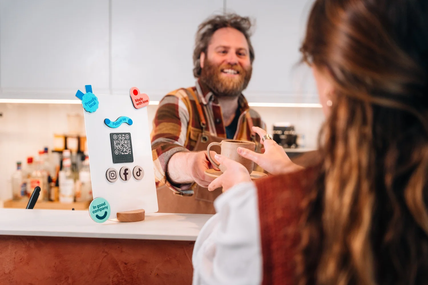 Barista servant un café à côté du présentoir connecté Smiirl, photo produit en situation