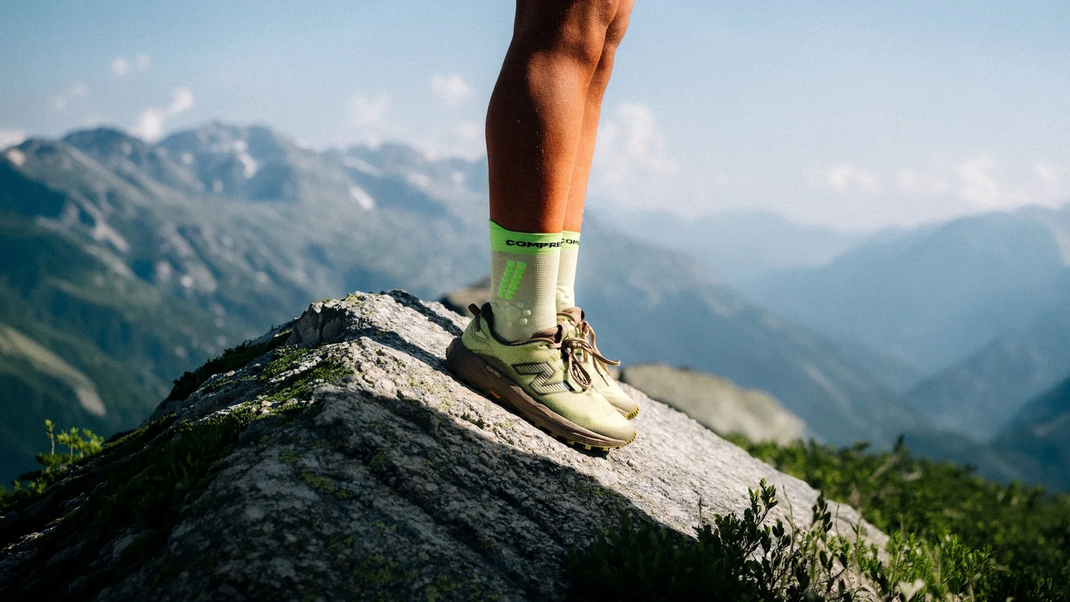 Traileur en New Balance debout sur un rocher face aux montagnes, campagne trail outdoor