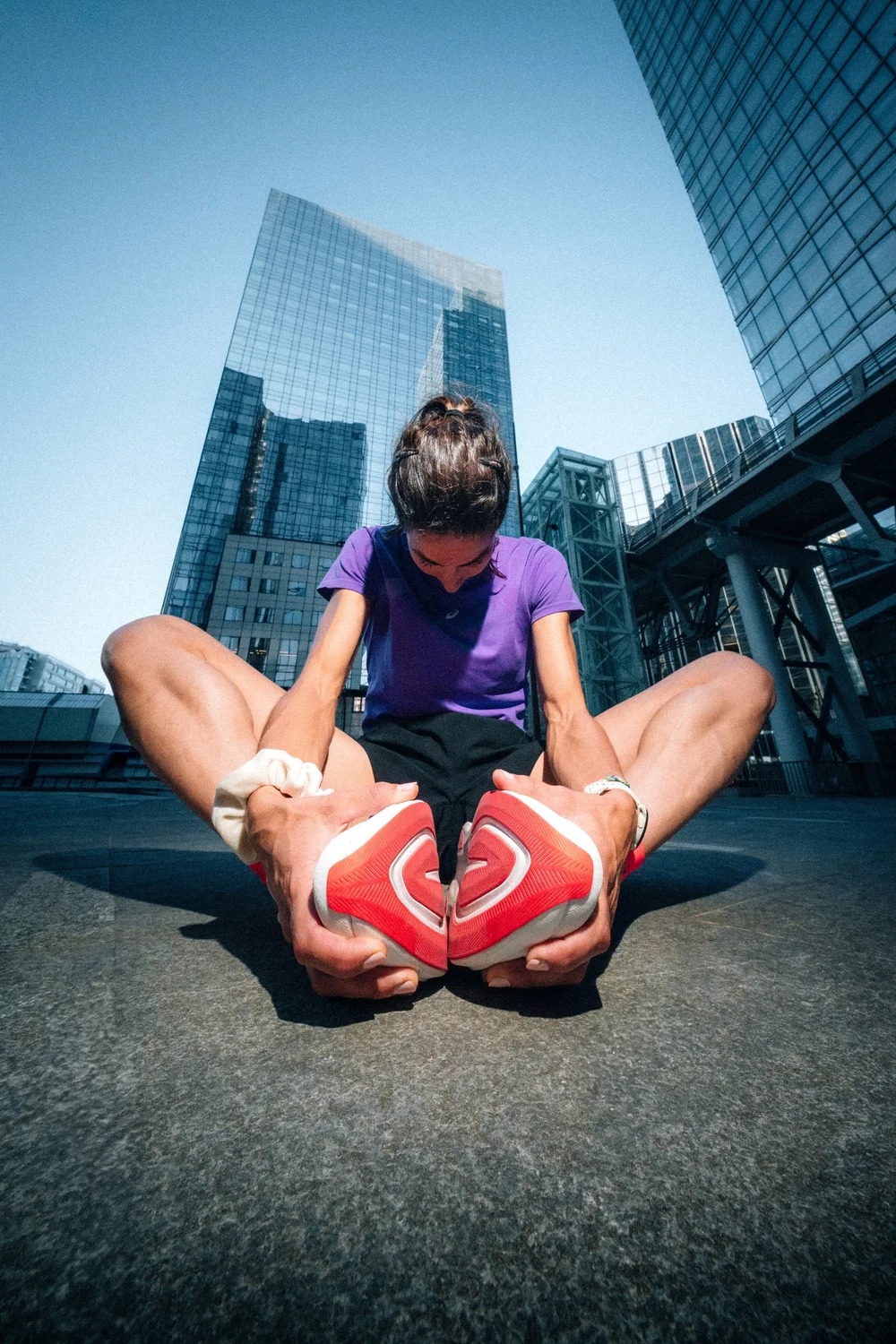 Coureuse ASICS qui s'étire au pied de tours de verre, photographie d'échauffement avant une course