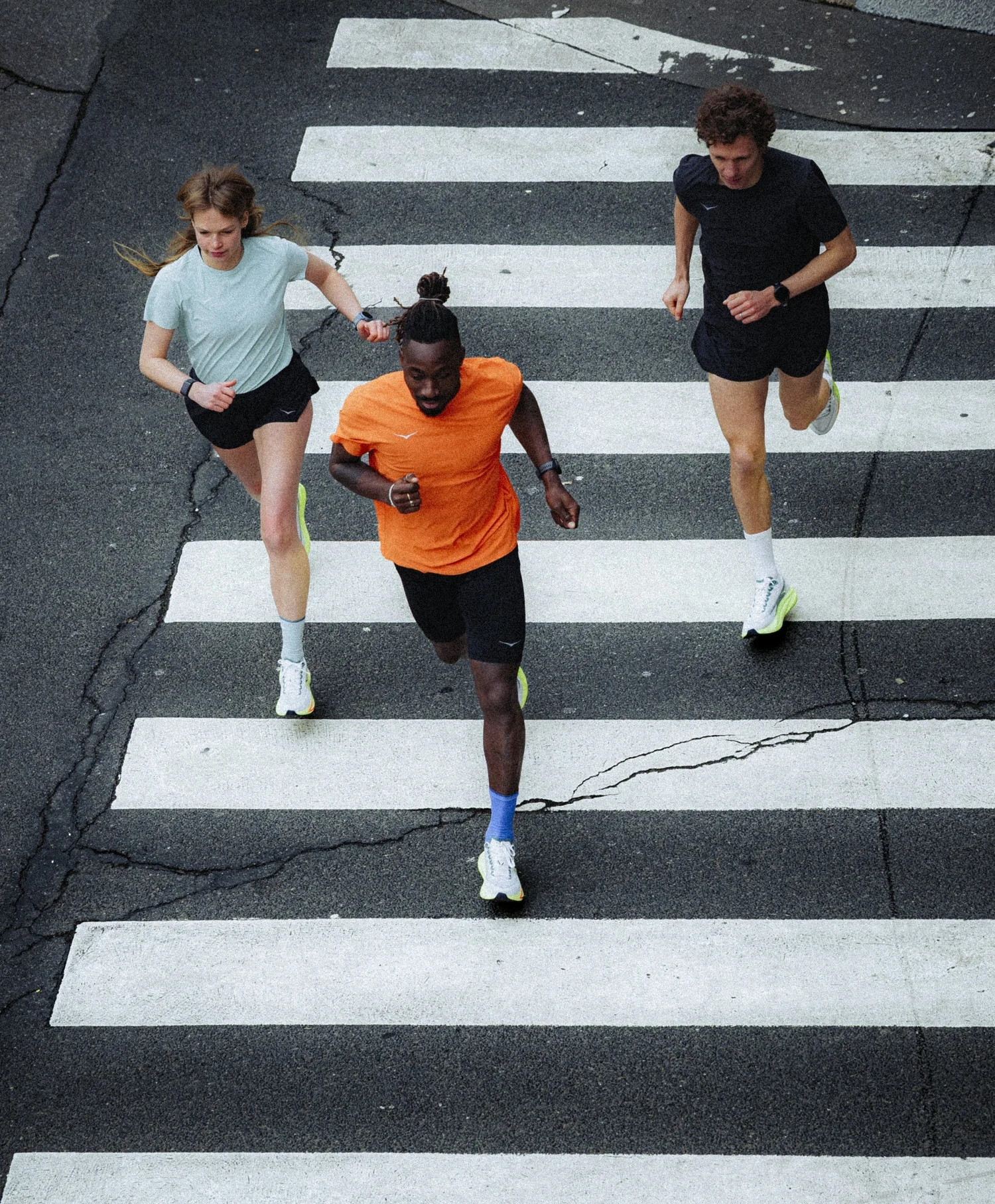 Trois coureurs en HOKA traversant un passage piéton vu d'en haut, campagne de lancement running