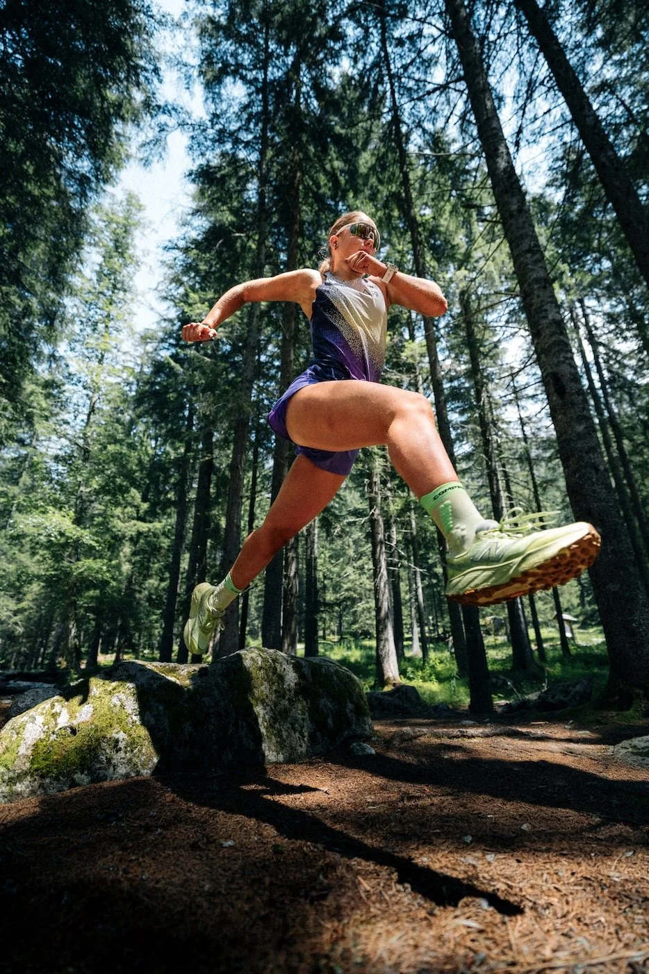 Traileuse en plein saut sur un sentier en forêt de montagne, photographie de trail en mouvement