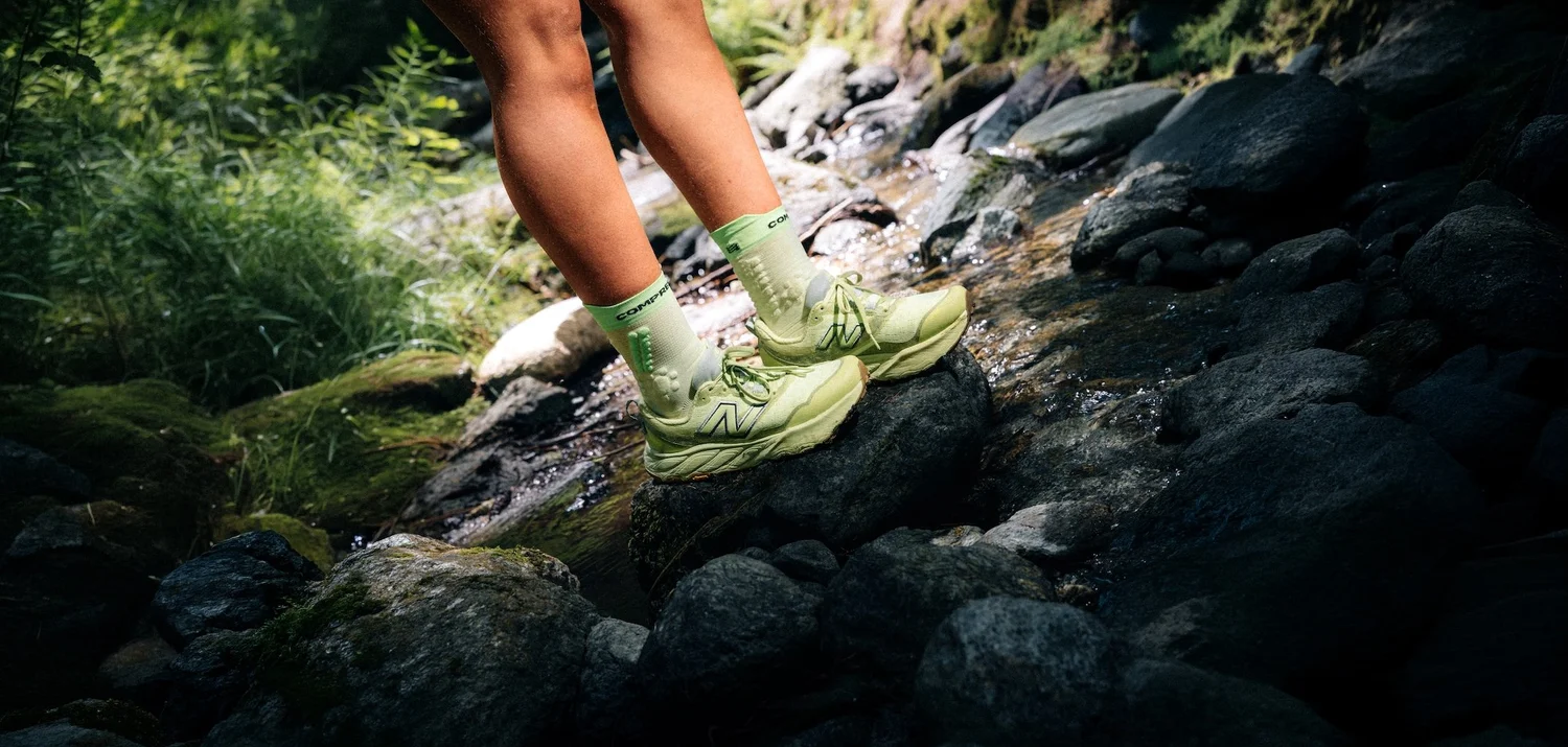 Pieds d'une traileuse en New Balance sur des rochers moussus, photographie de trail