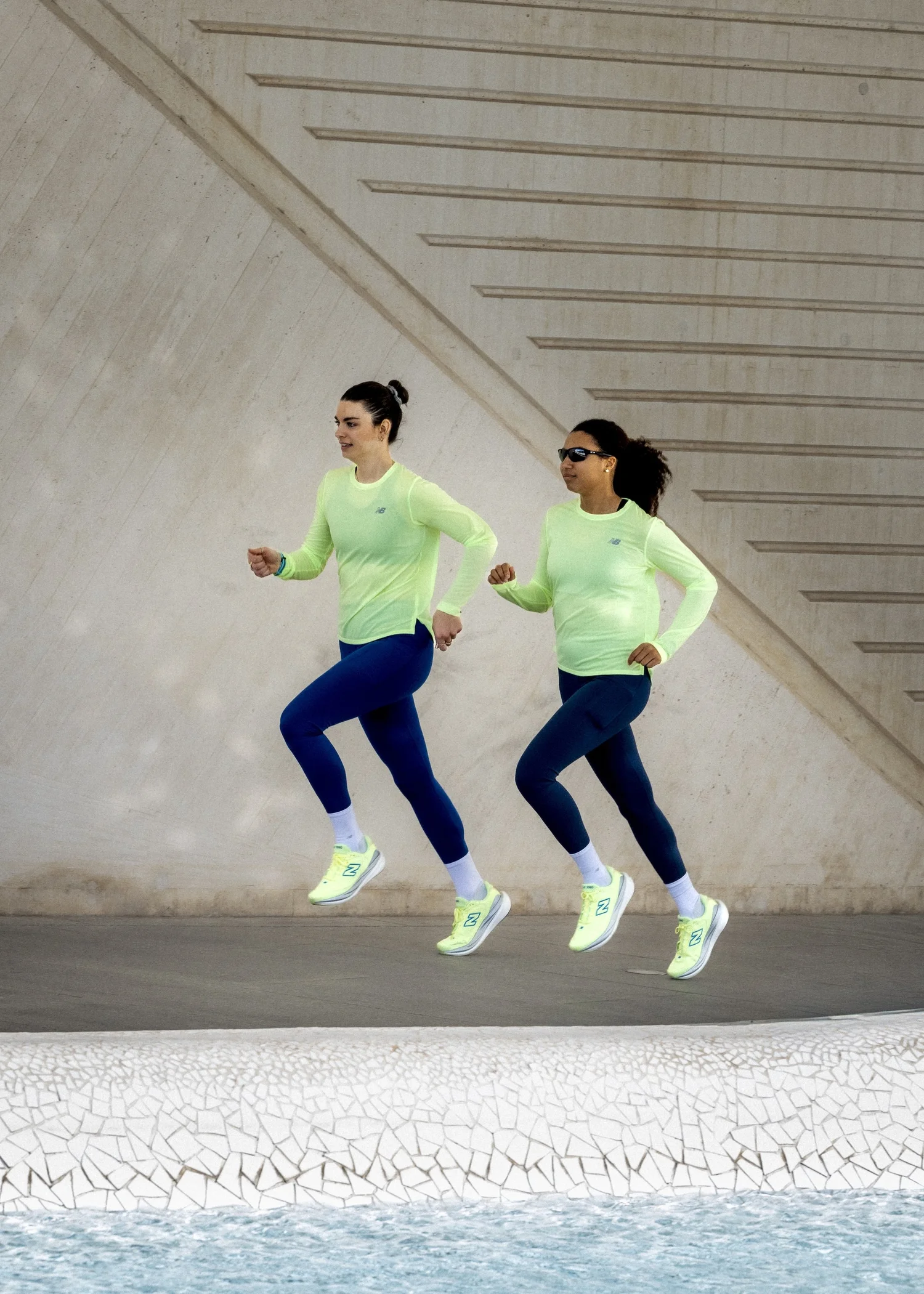 Deux coureuses en New Balance qui sautent devant une architecture blanche, campagne marathon à Valence