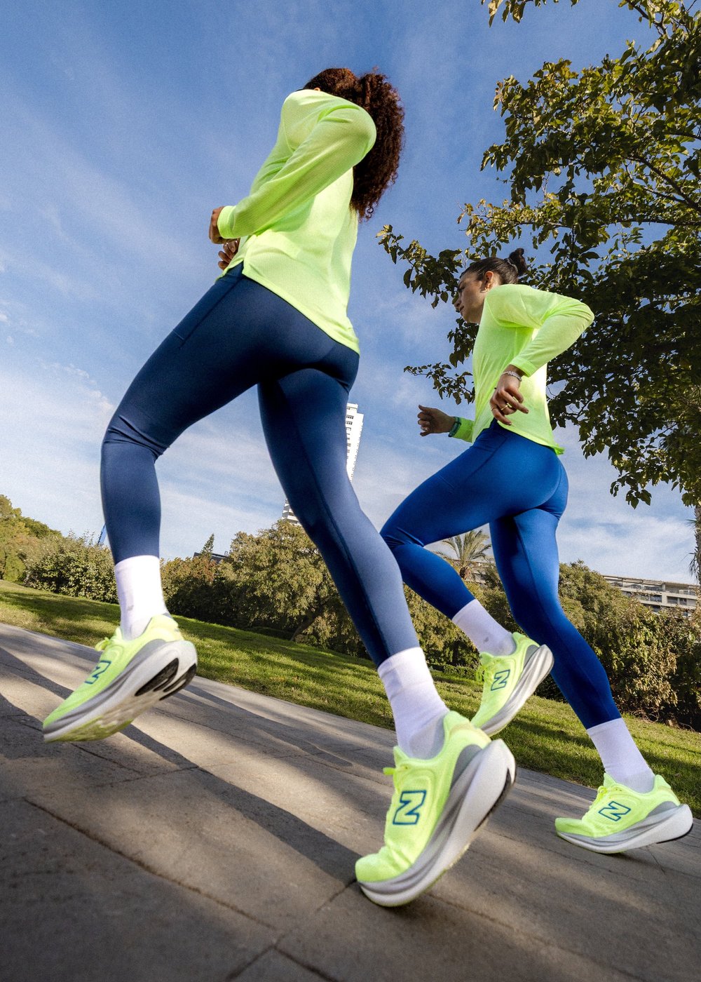 Deux coureuses en New Balance photographiées en contre-plongée sous un ciel bleu, campagne running en plein soleil