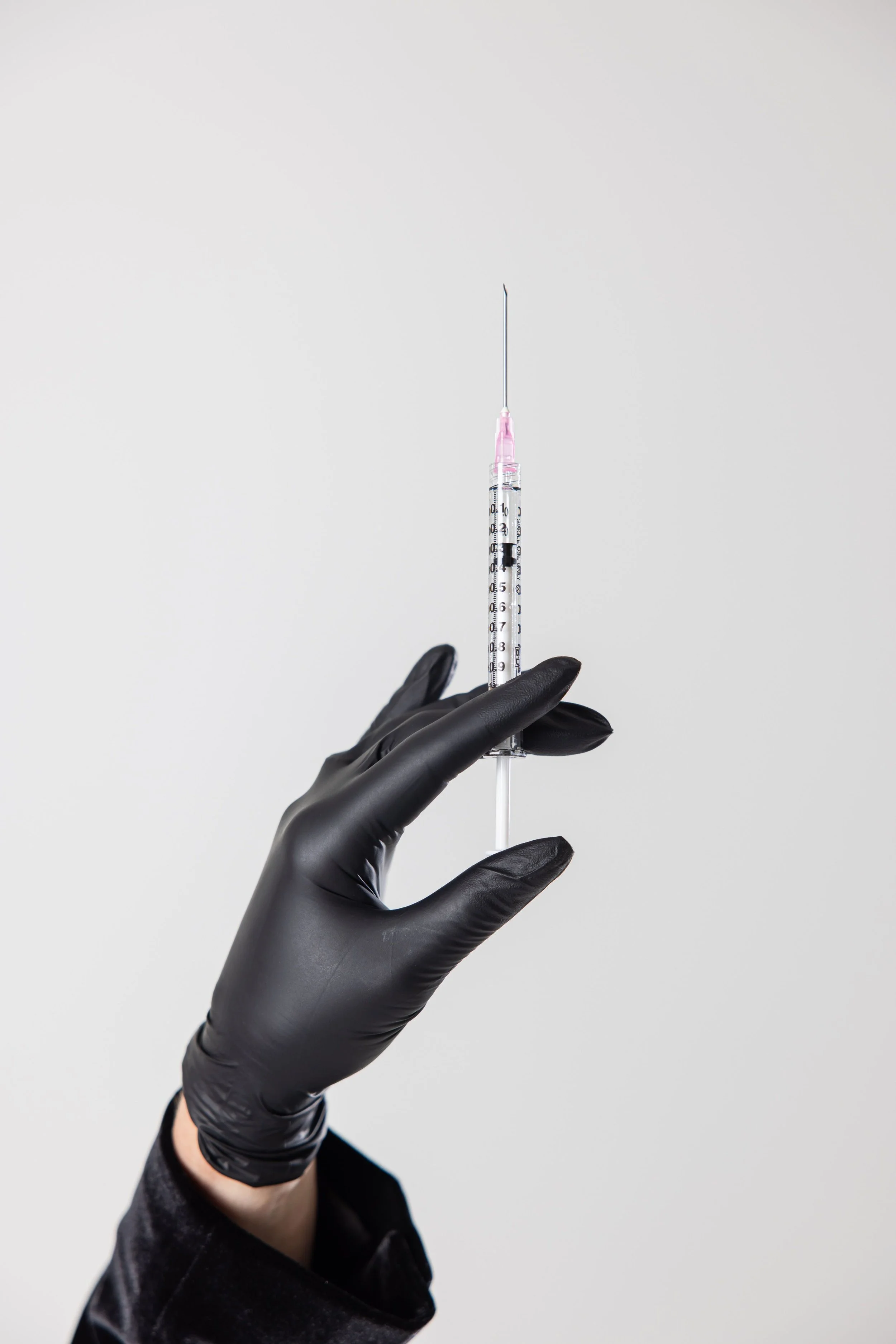 Gloved hand holding a syringe with a needle and pink cap