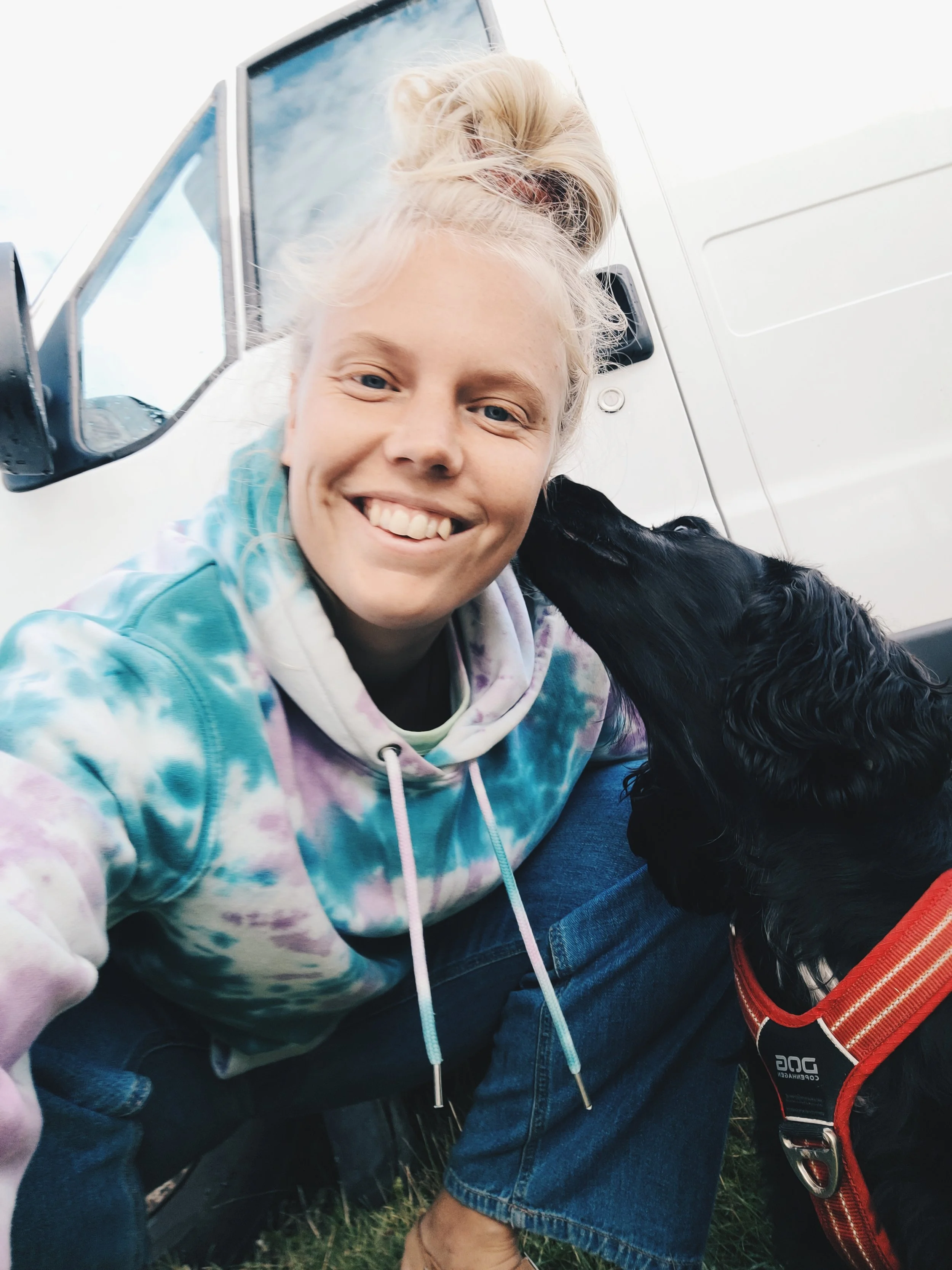 Johanna i sin färgglada batiktröja, tillsammans med sin hund som slickar henne i asiktet,