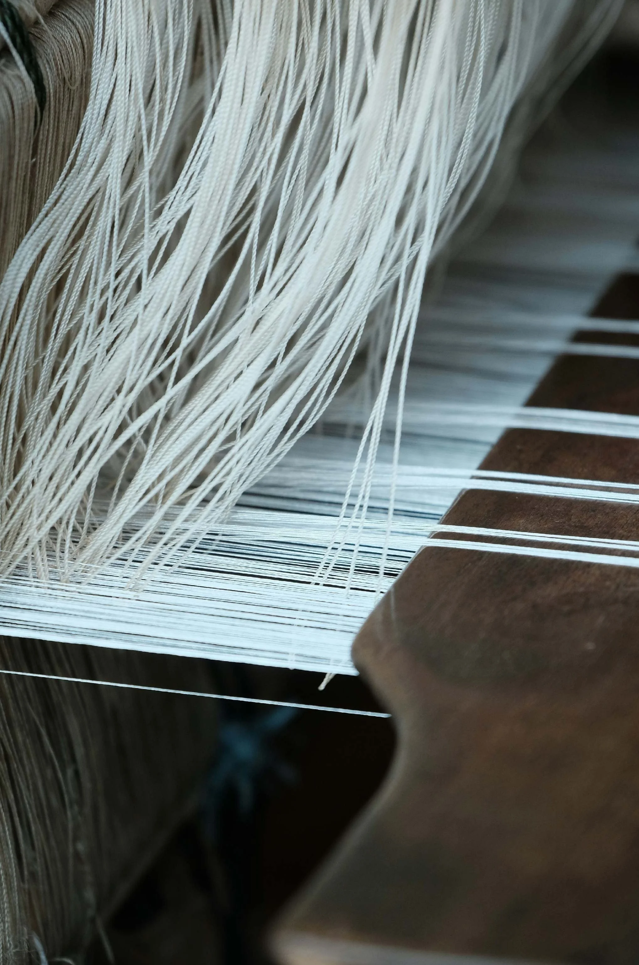 Close-up of white threads on a wooden frame weaving loom.