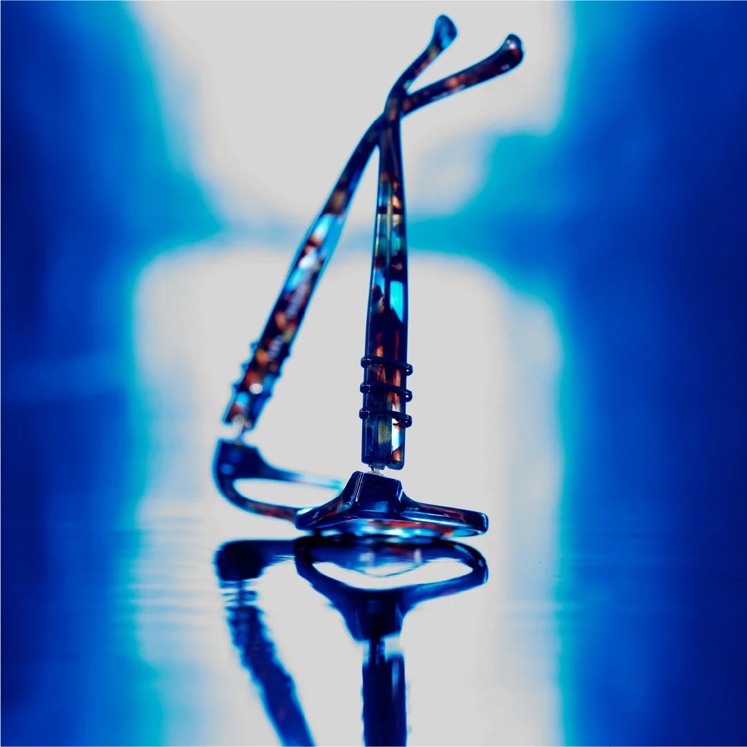 A pair of eyeglasses with tortoiseshell frames resting on a reflective surface under blue lighting.