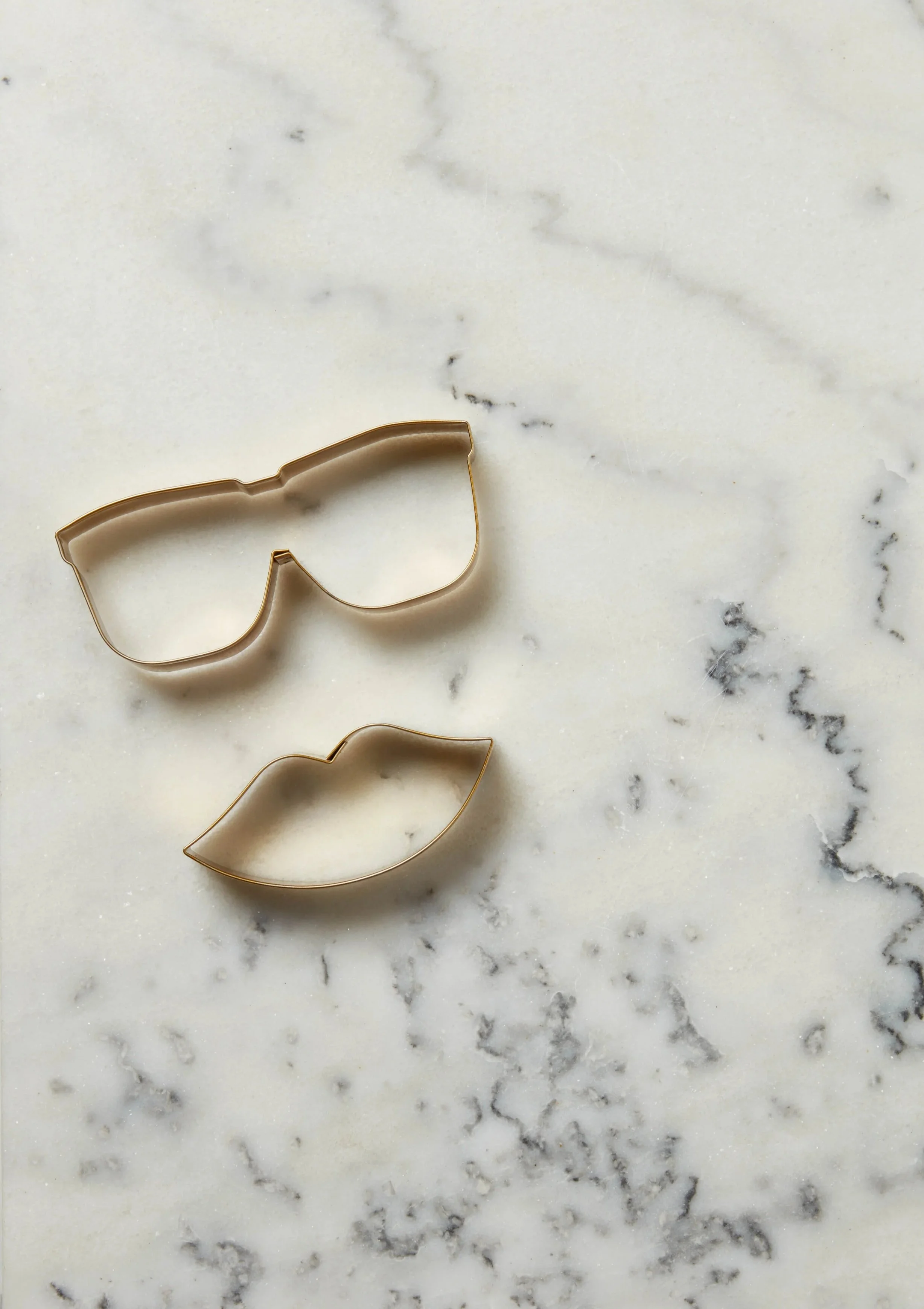 Cookie cutter shaped like sunglasses and lips on a white marble surface.