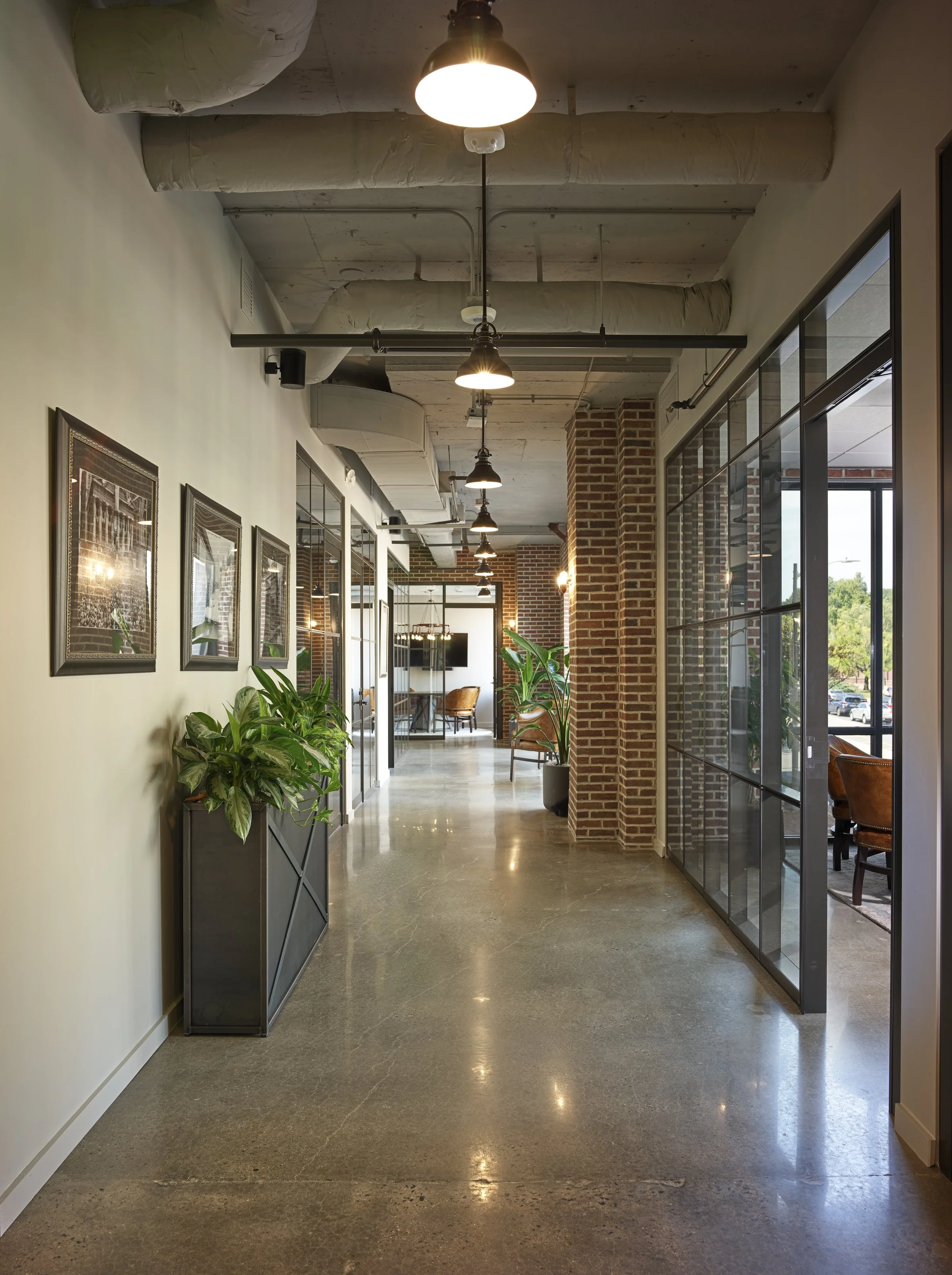 Long one-point perspective image looking down a hallway featuring conference rooms and large windows 