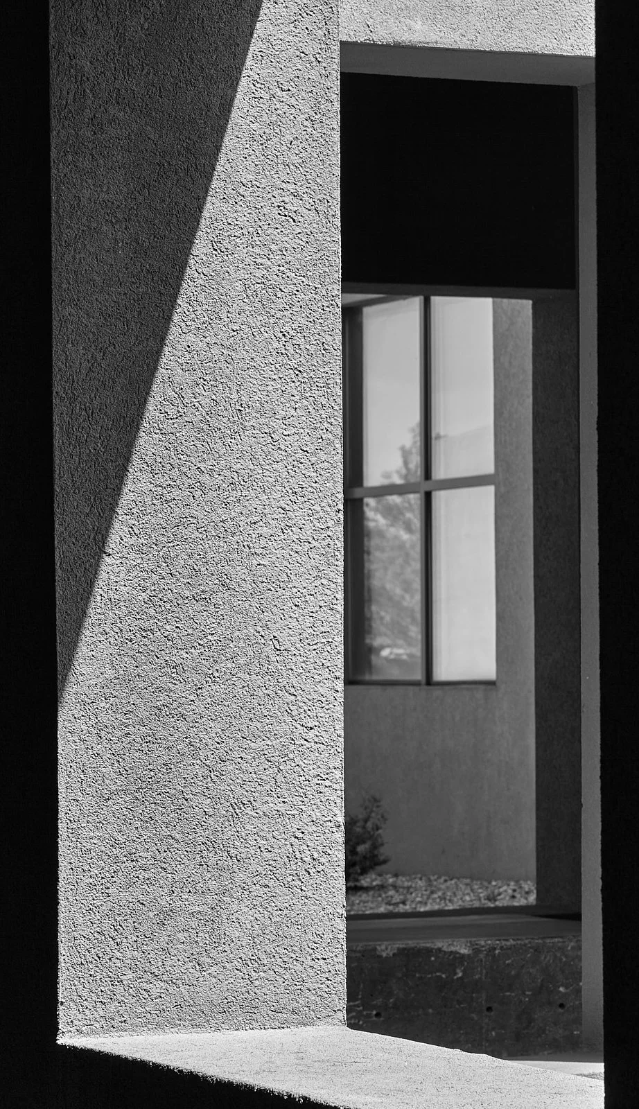 Black and white photo of a building facade with a textured wall, window, and shadow.