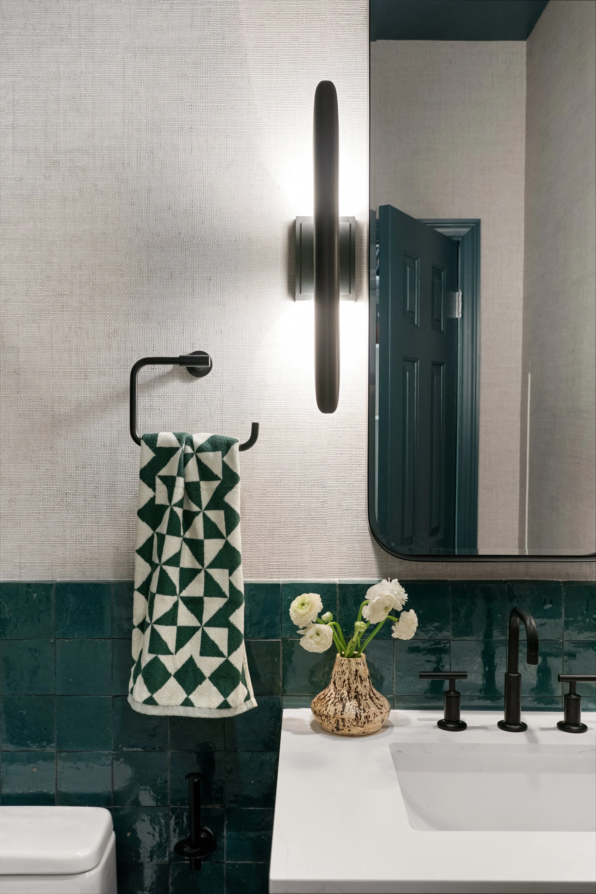 Modern secondary bathroom featuring deep green zellige tile, textured wallpaper, minimalist black hardware, and a pill-shaped mirror in a Jersey City residence.