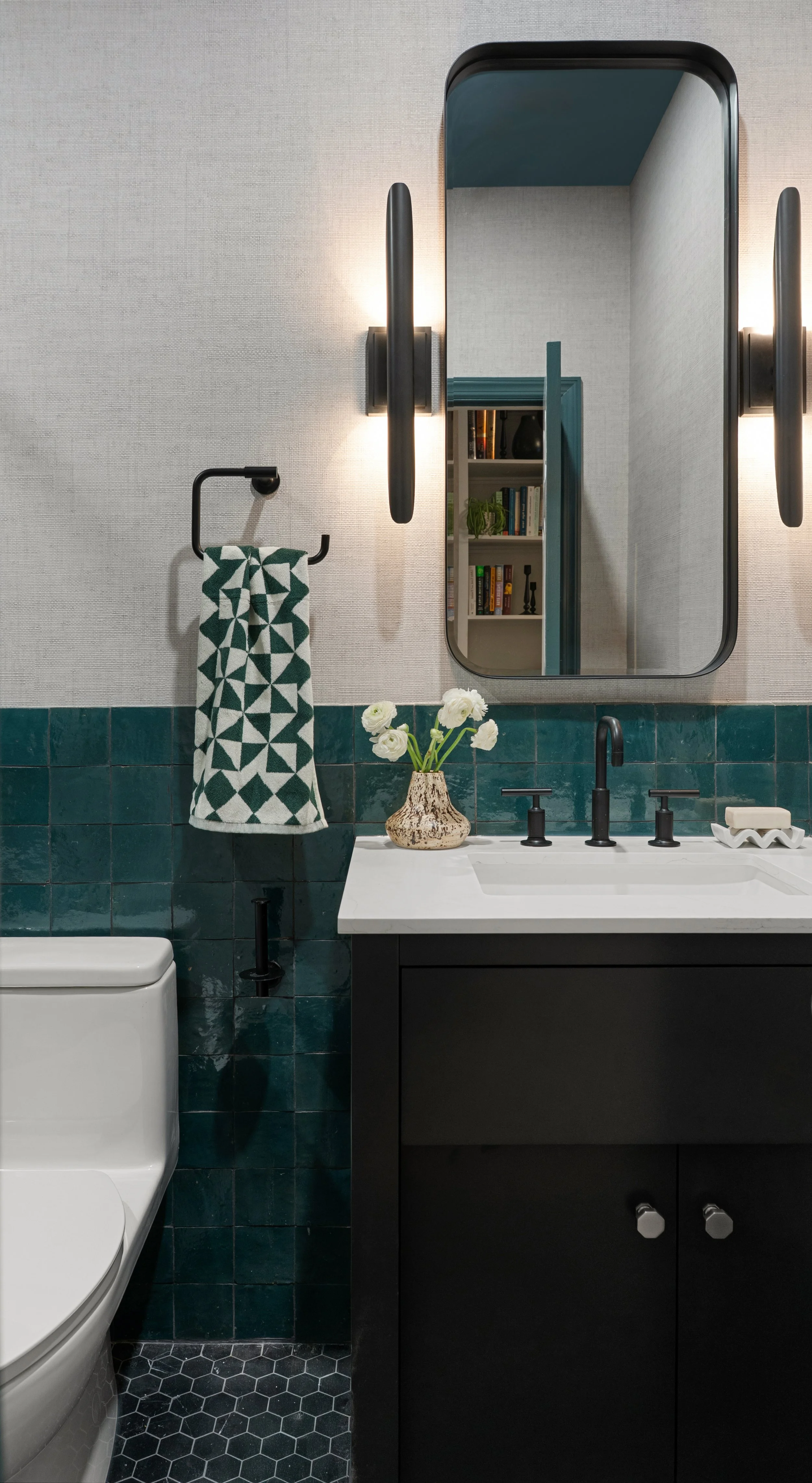 Modern secondary bathroom featuring deep green zellige tile, textured wallpaper, minimalist black hardware, and a pill-shaped mirror in a Jersey City residence.