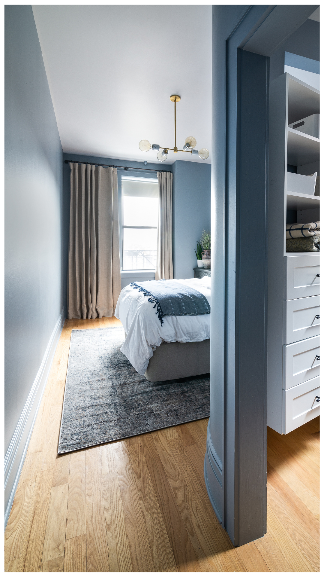 A 5-star residential retreat featuring a curved architectural partition in dusty blue, textured designer wallcovering, and a modern brass chandelier, engineered to integrate a luxury walk-in closet within the existing footprint.