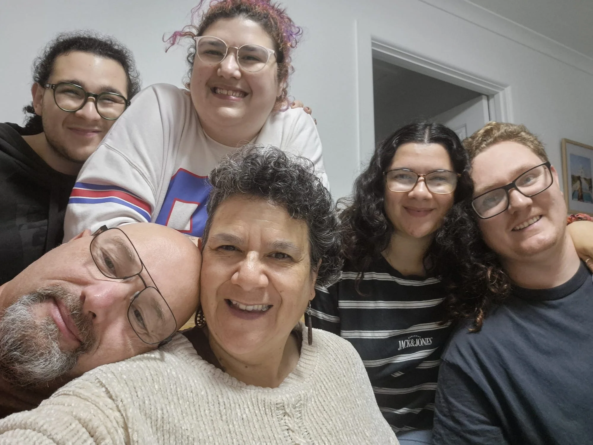 Group selfie of six smiling people indoors.