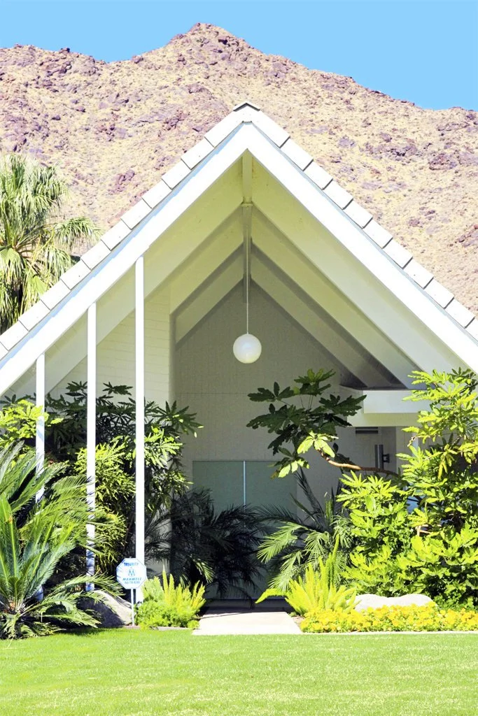 A-frame house with lush green landscaping against a mountainous backdrop.